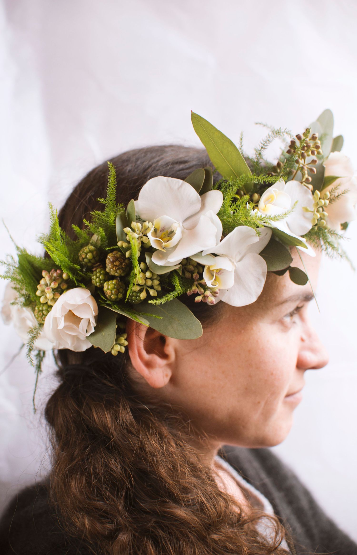 Woman wearing an elegant white orchid and green fern flower crown on dark hair.