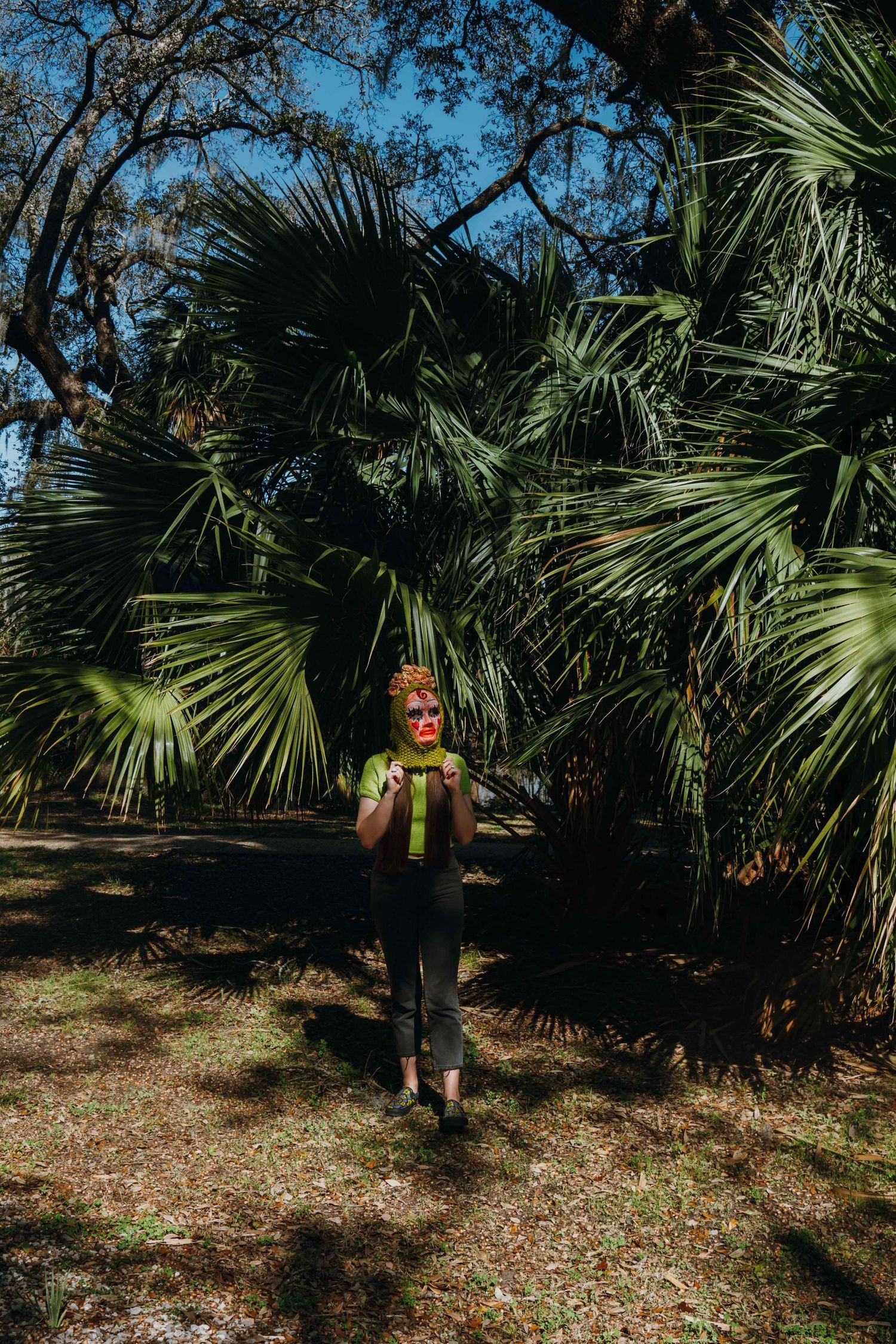 Woman in green outfit standing among tall palm trees in a sunny tropical park.