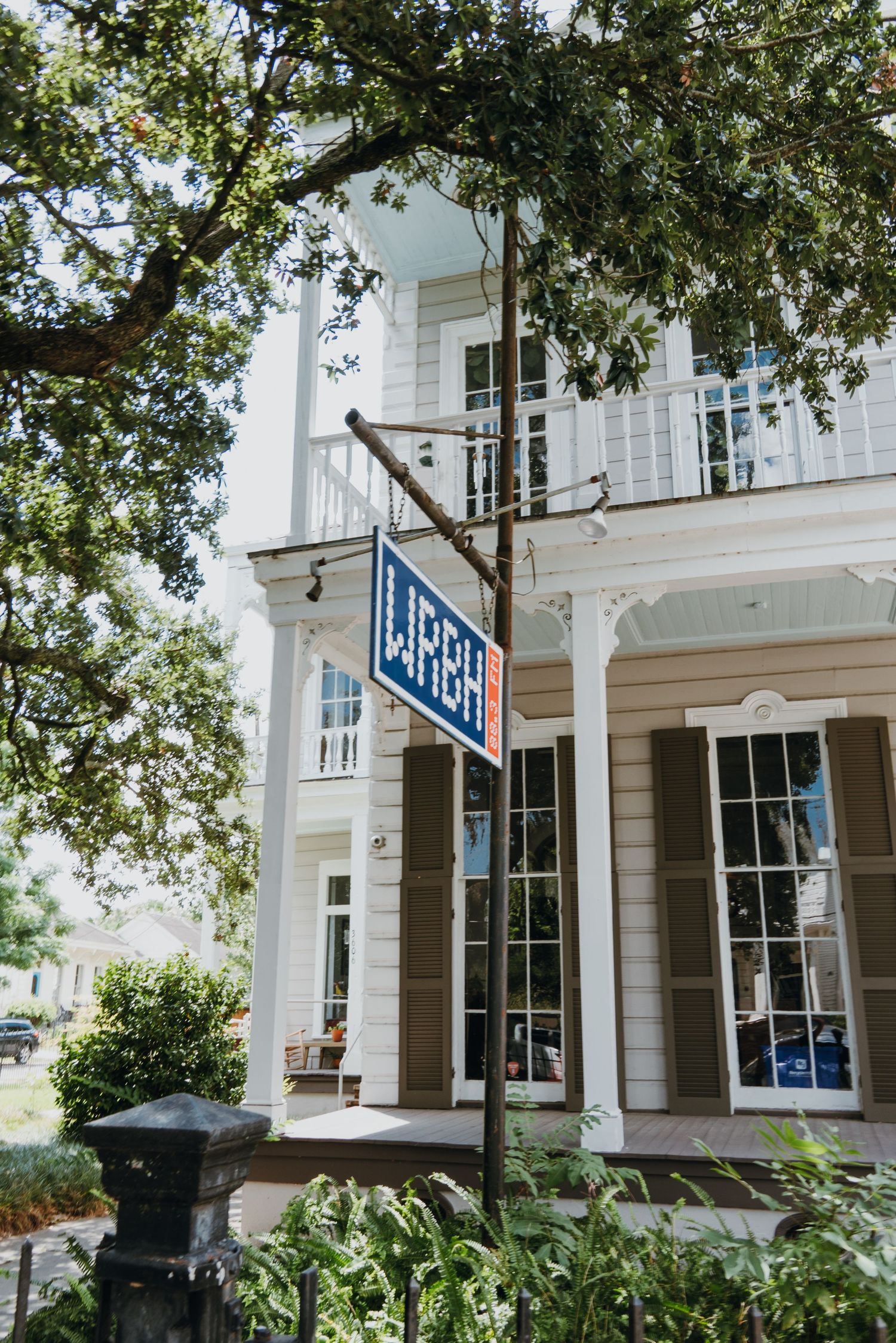 White two-story building with blue LUNCH sign on pole surrounded by green trees.