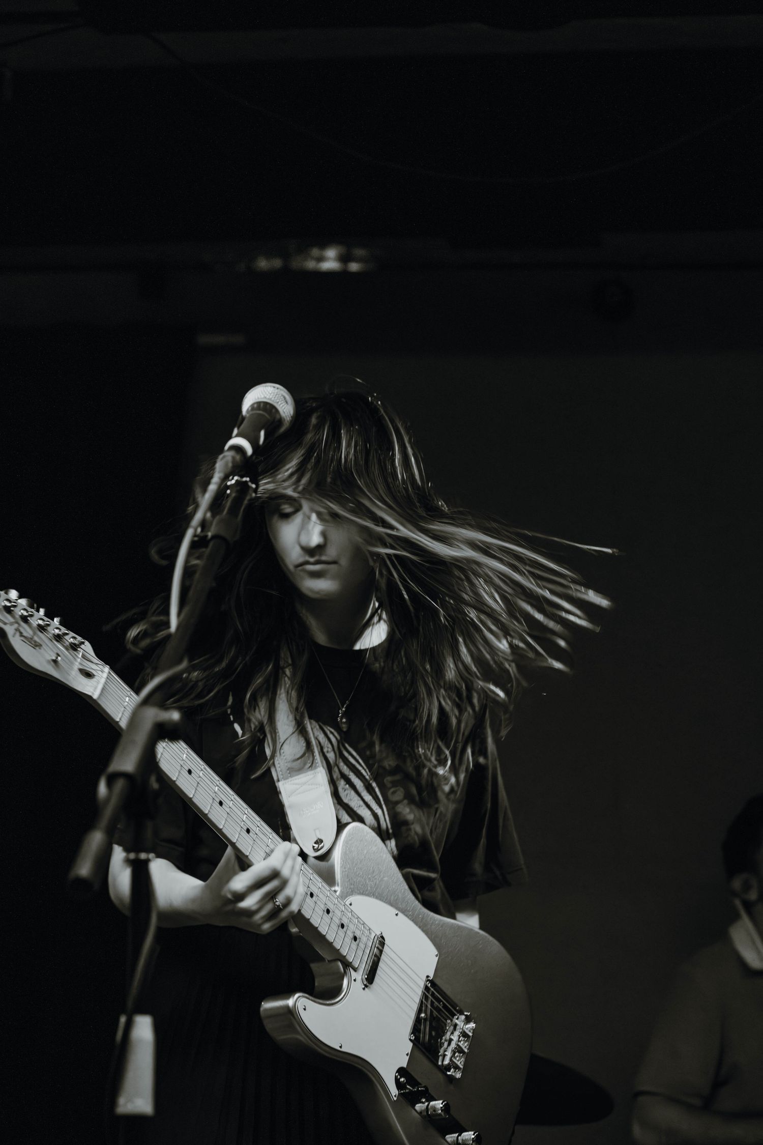 Black and white photo of a female guitarist with flowing hair playing electric guitar on stage.