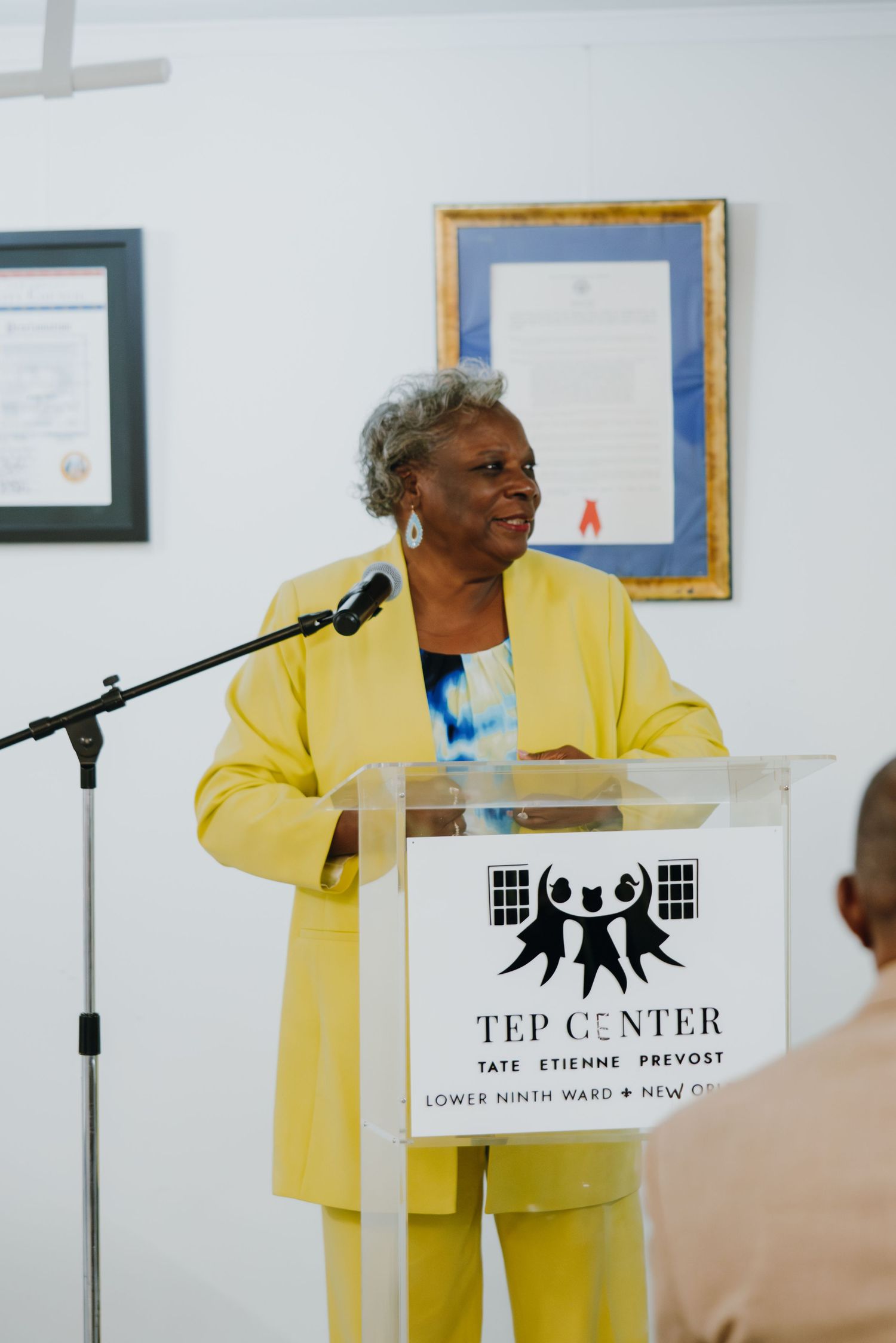 Woman in yellow suit speaking at TEP Center podium in Lower Ninth Ward New Orleans.