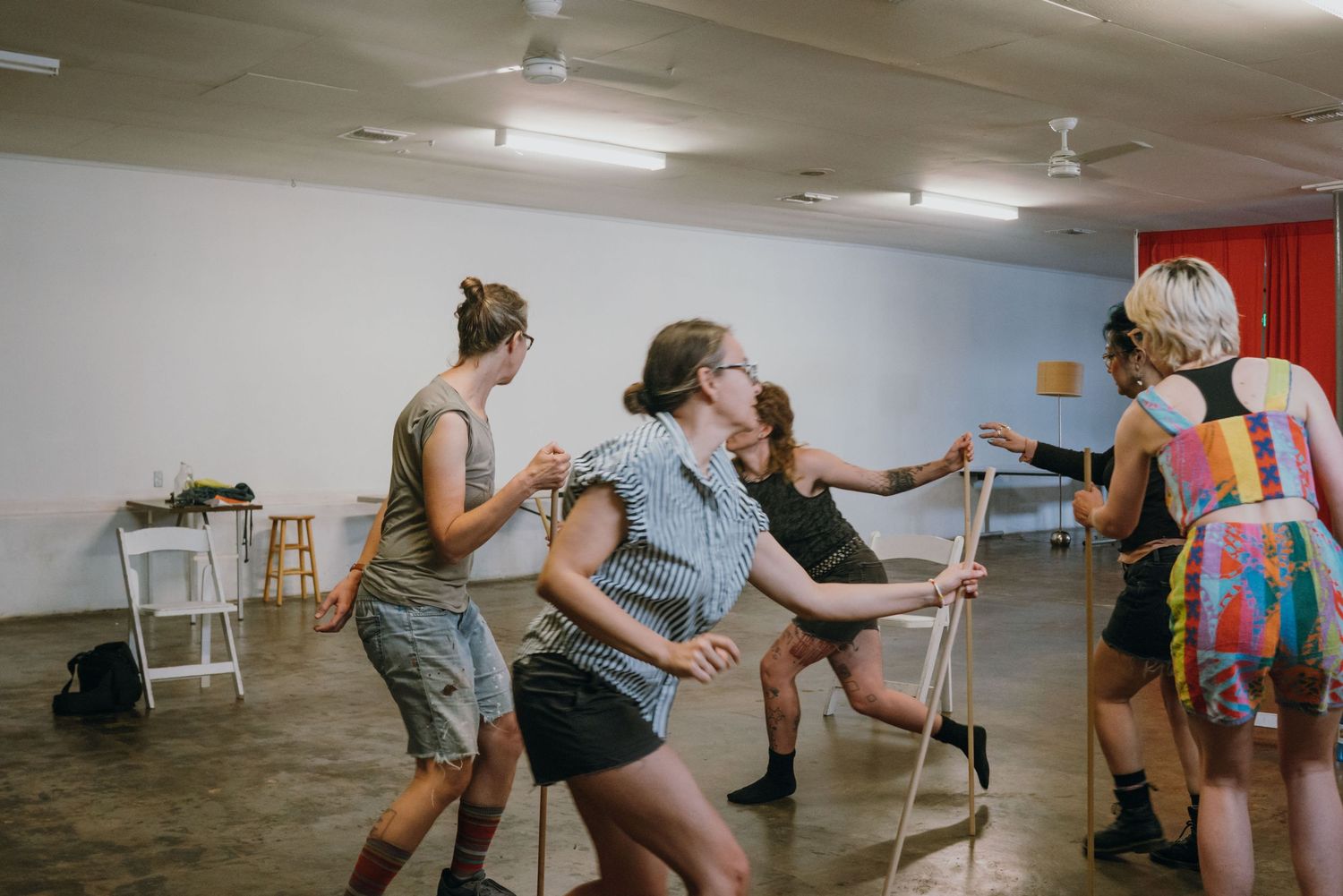 Group of performers practicing physical theater exercises with wooden sticks in a rehearsal space.