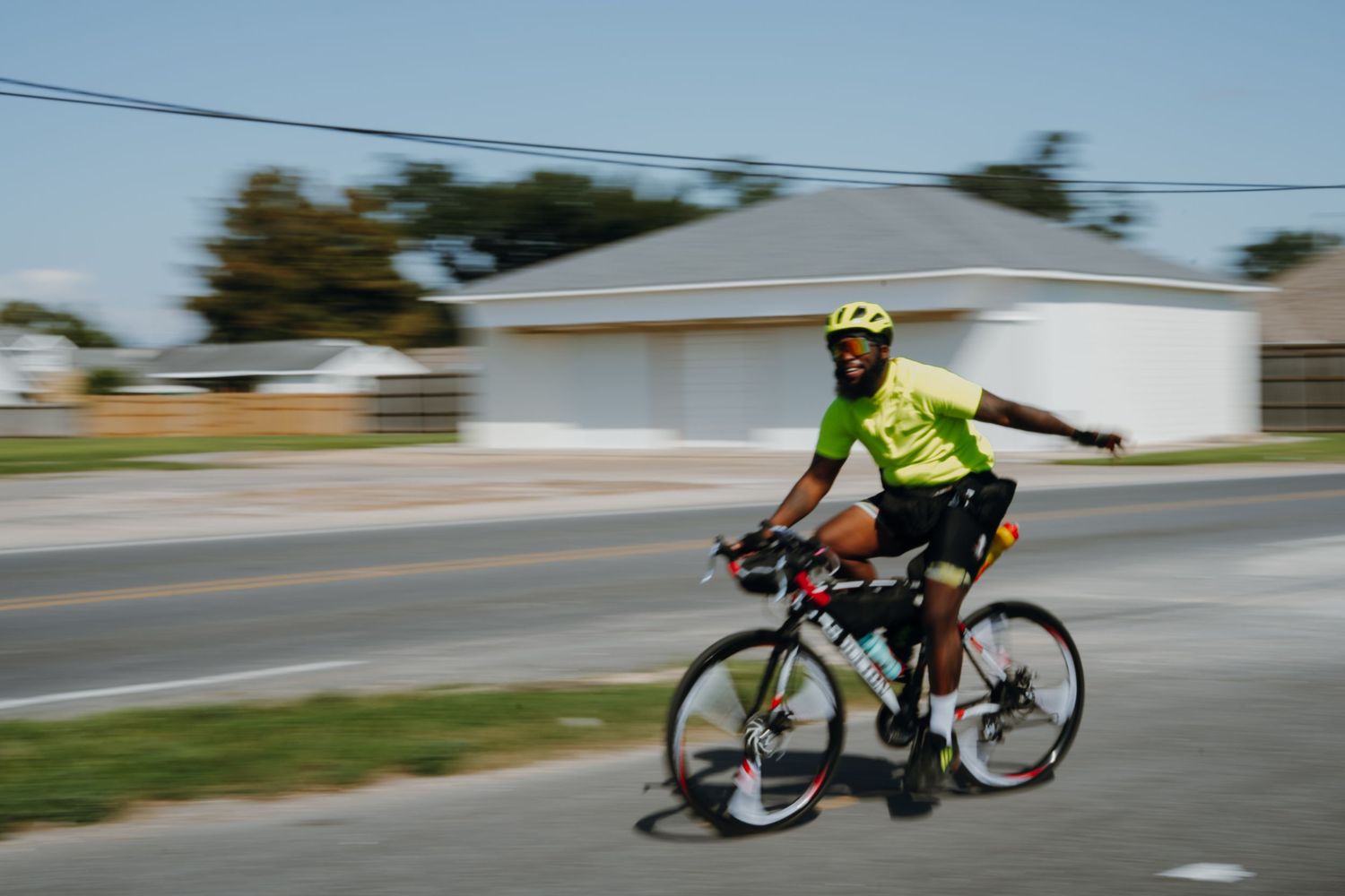 Cyclist in neon yellow jersey riding at speed along a suburban road on a clear day.