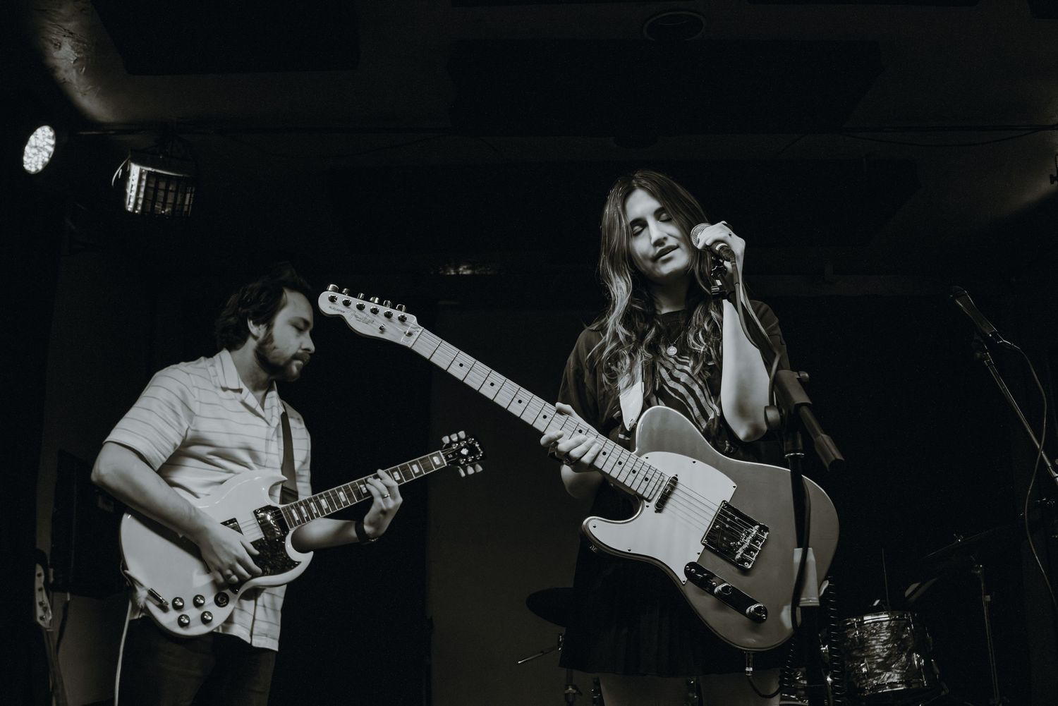 Black and white photo of two musicians playing electric guitars on stage at a live music venue.