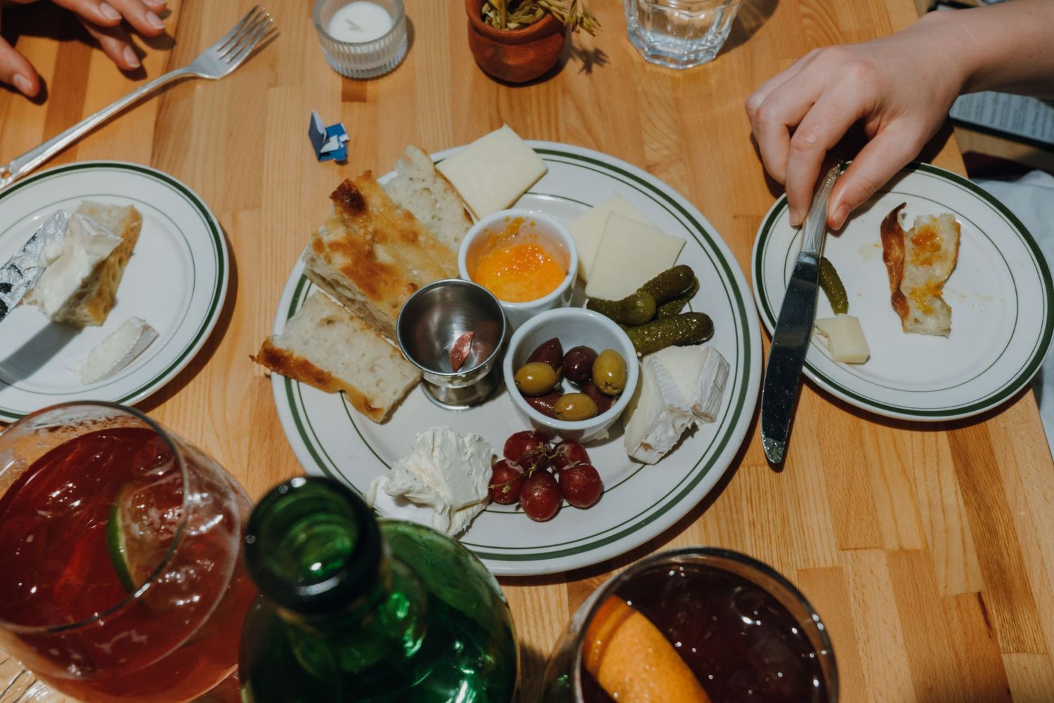 Charcuterie board with cheese, olives, pickles, and jam served on a white plate at a restaurant table.