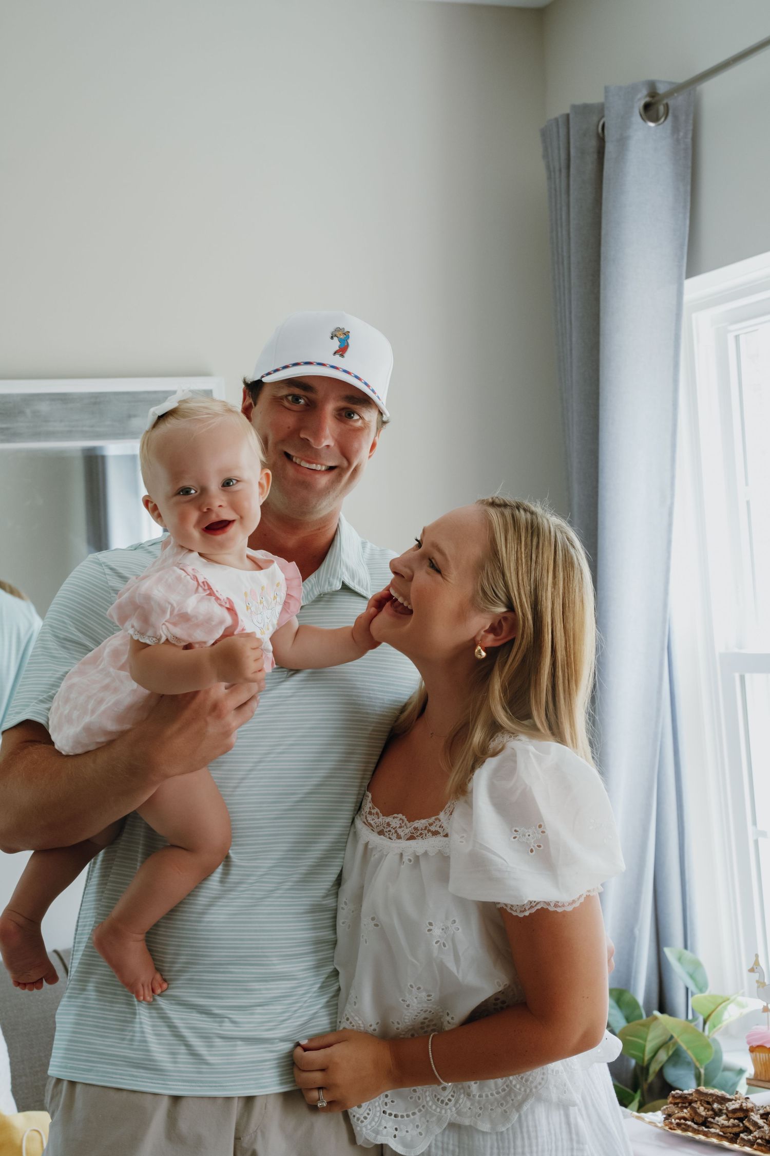 Happy family with father in white cap holding baby girl at a birthday celebration indoors.