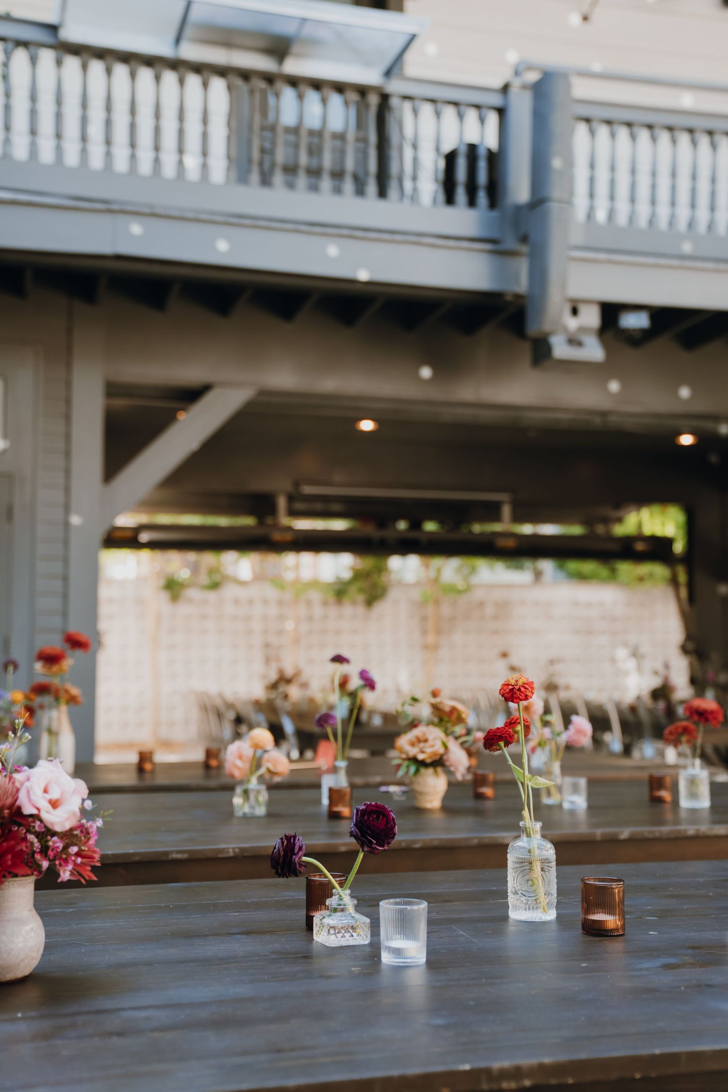 Elegant outdoor wedding reception tables with colorful wildflower bud vases and candles.