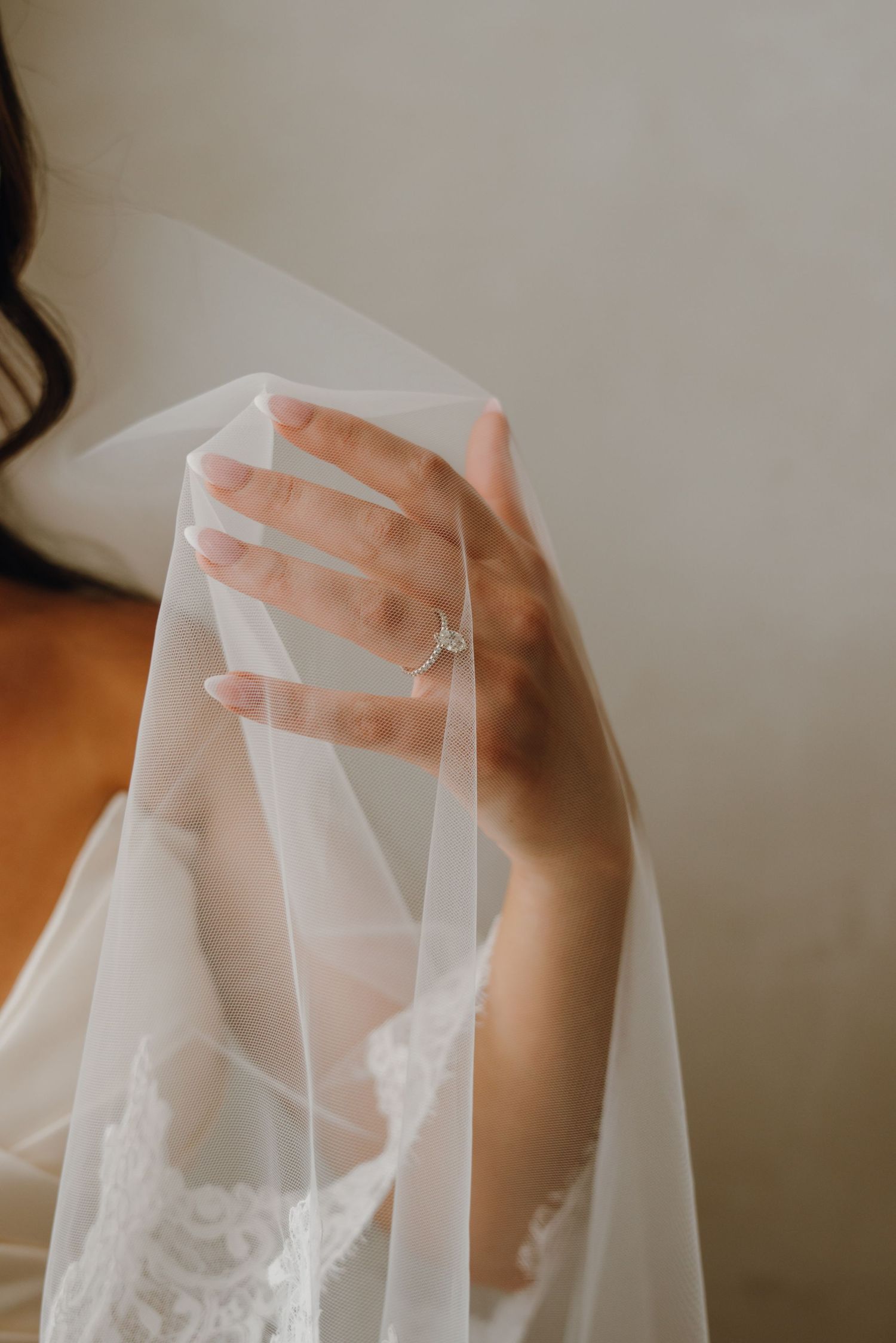 Bride lifting her delicate veil to reveal a sparkling diamond engagement ring on her hand.