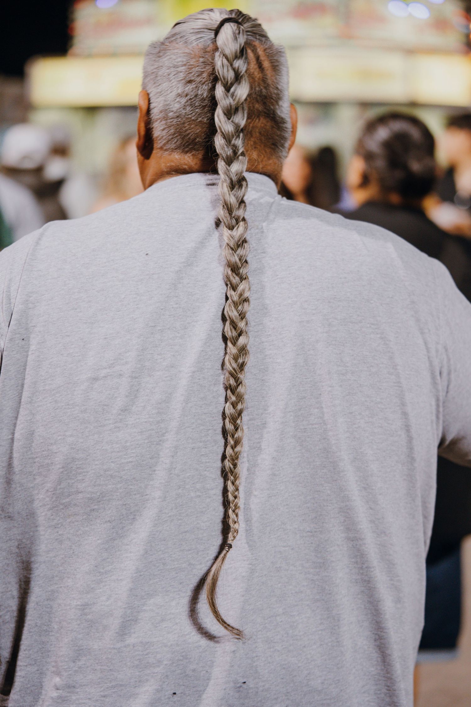 Man with long gray braided hair down his back wearing a gray t-shirt at outdoor event.