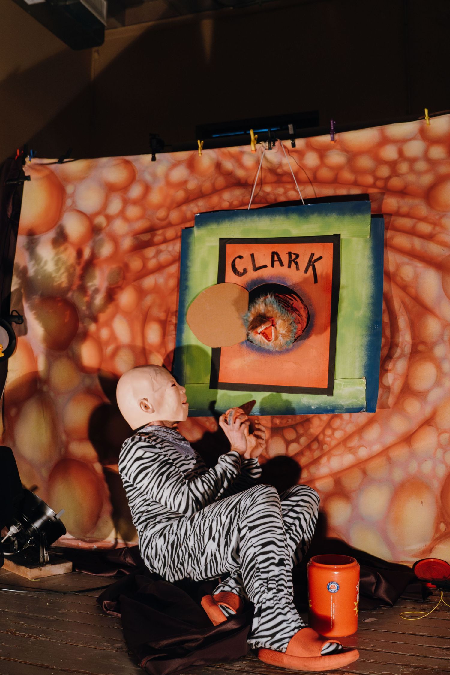 Performer in zebra costume holds cat near colorful Clark puppet show backdrop.