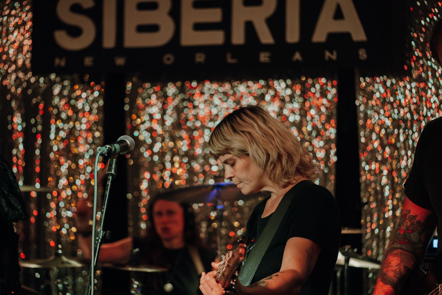 Guitarist performing on stage at Siberia New Orleans venue with colorful bokeh lights in background.