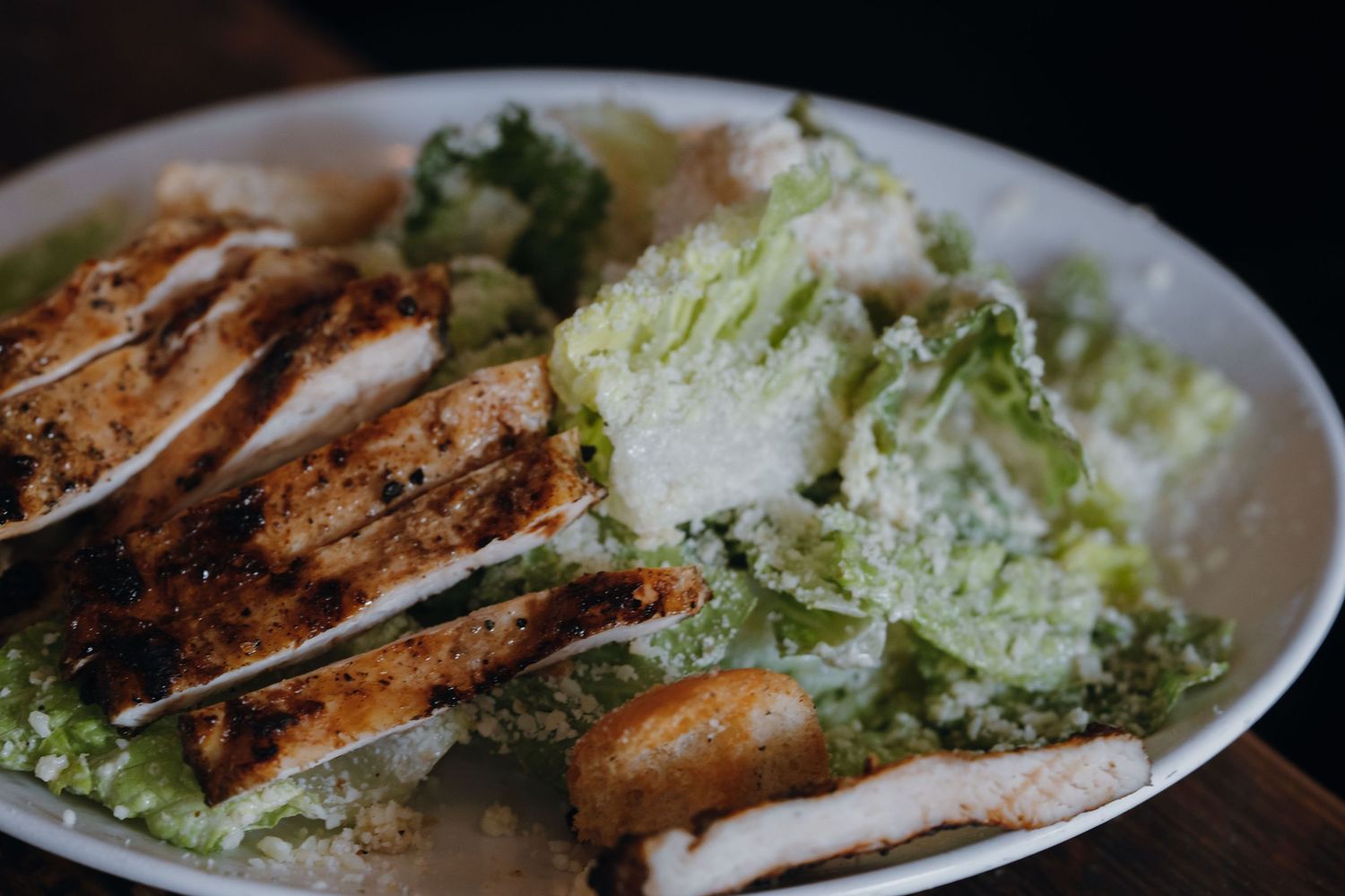Grilled chicken Caesar salad with romaine lettuce, croutons, and creamy dressing served on a white plate.