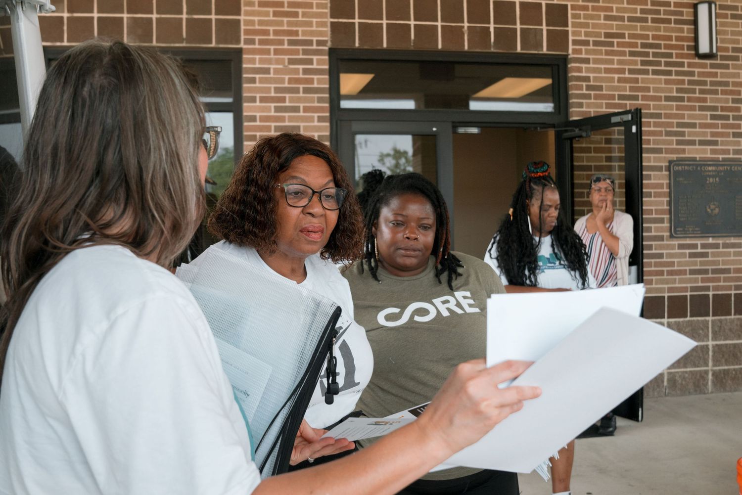CORE organization members reviewing documents outside a brick building at a community event.