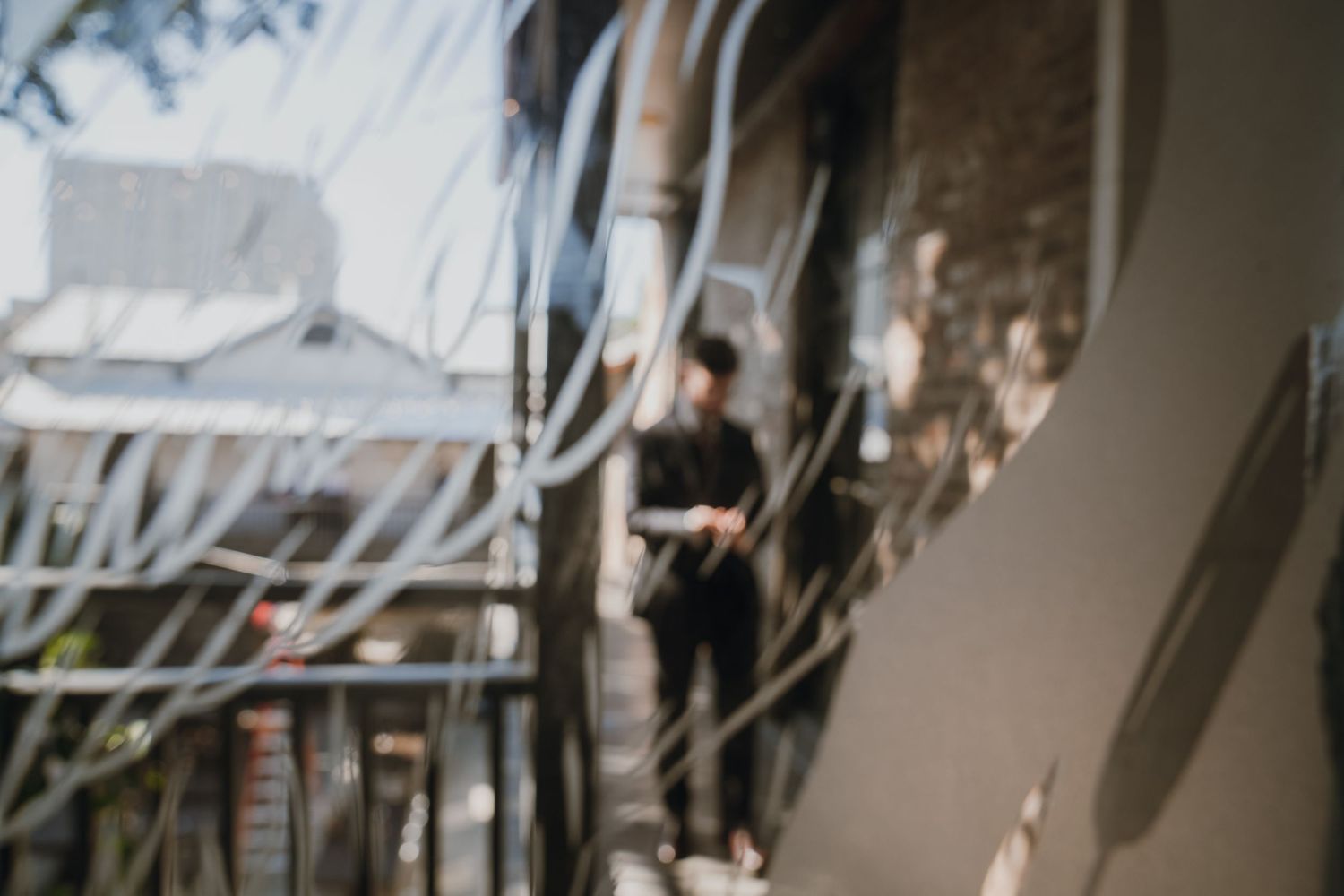Blurred artistic photo of man on balcony surrounded by tangled wires outdoors.