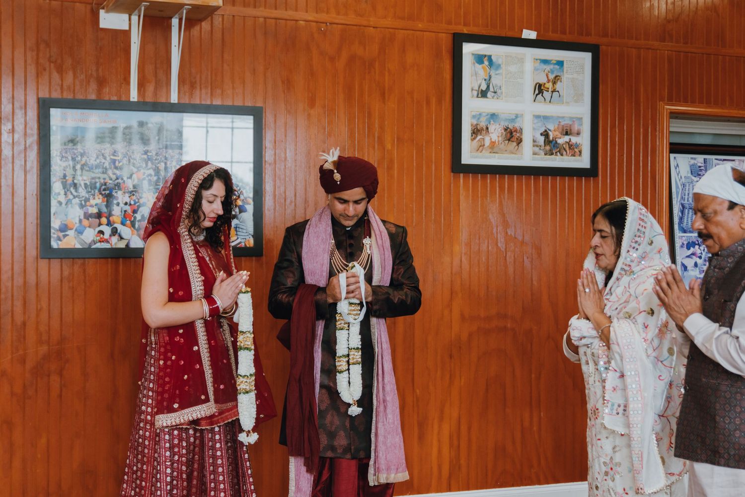 Sikh bride and groom in traditional red attire exchange garlands during an Anand Karaj wedding ceremony.