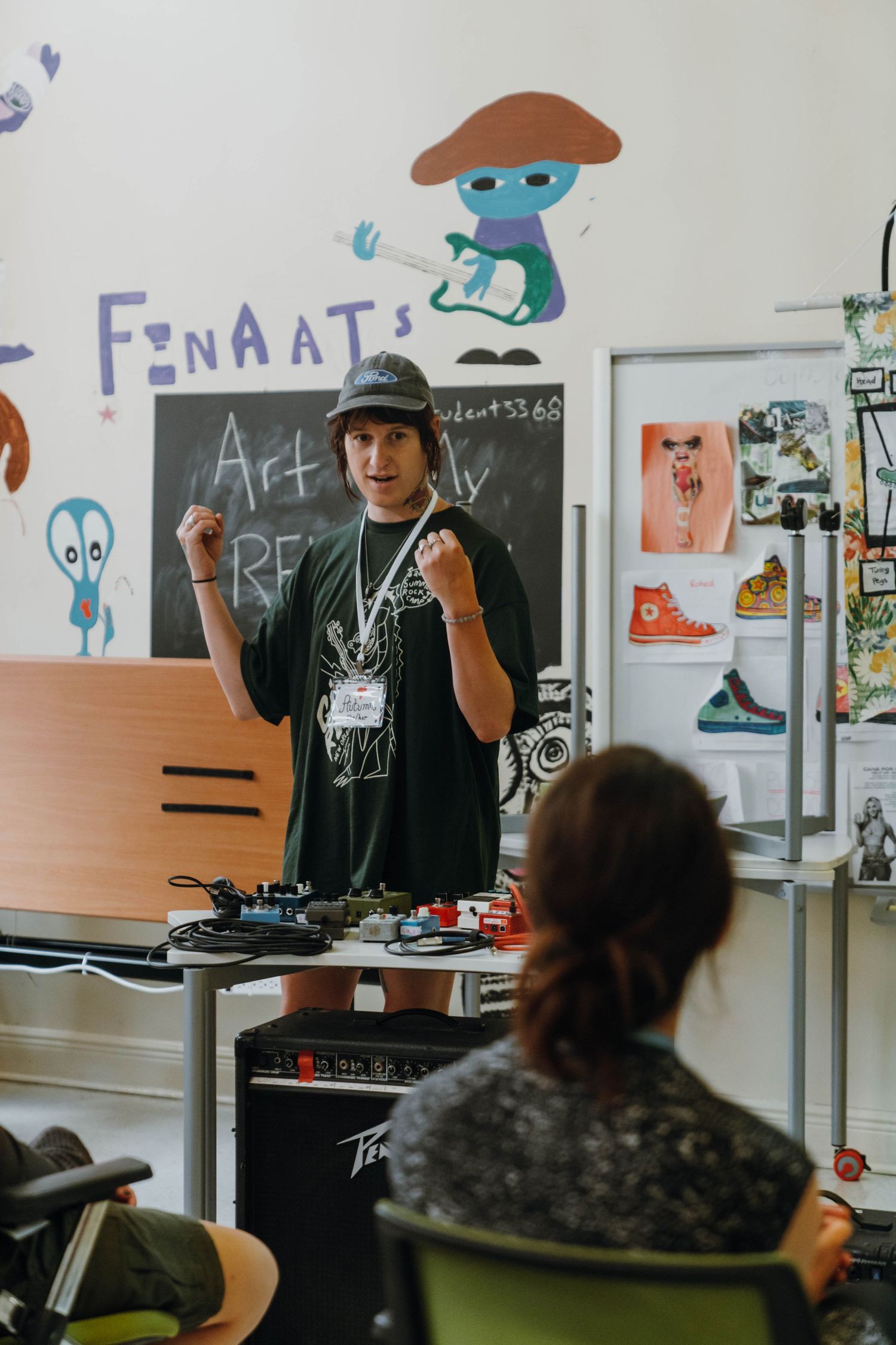 Young instructor with cap and lanyard presents energetically before chalkboard in colorful art classroom. New Orleans, Louisiana, Mississipp