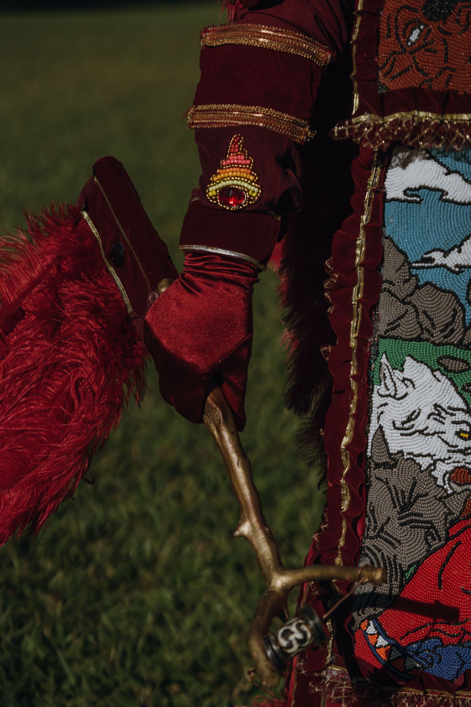 Close-up of Mardi Gras Indian holding a wooden stick wearing red gloves and beaded costume details.