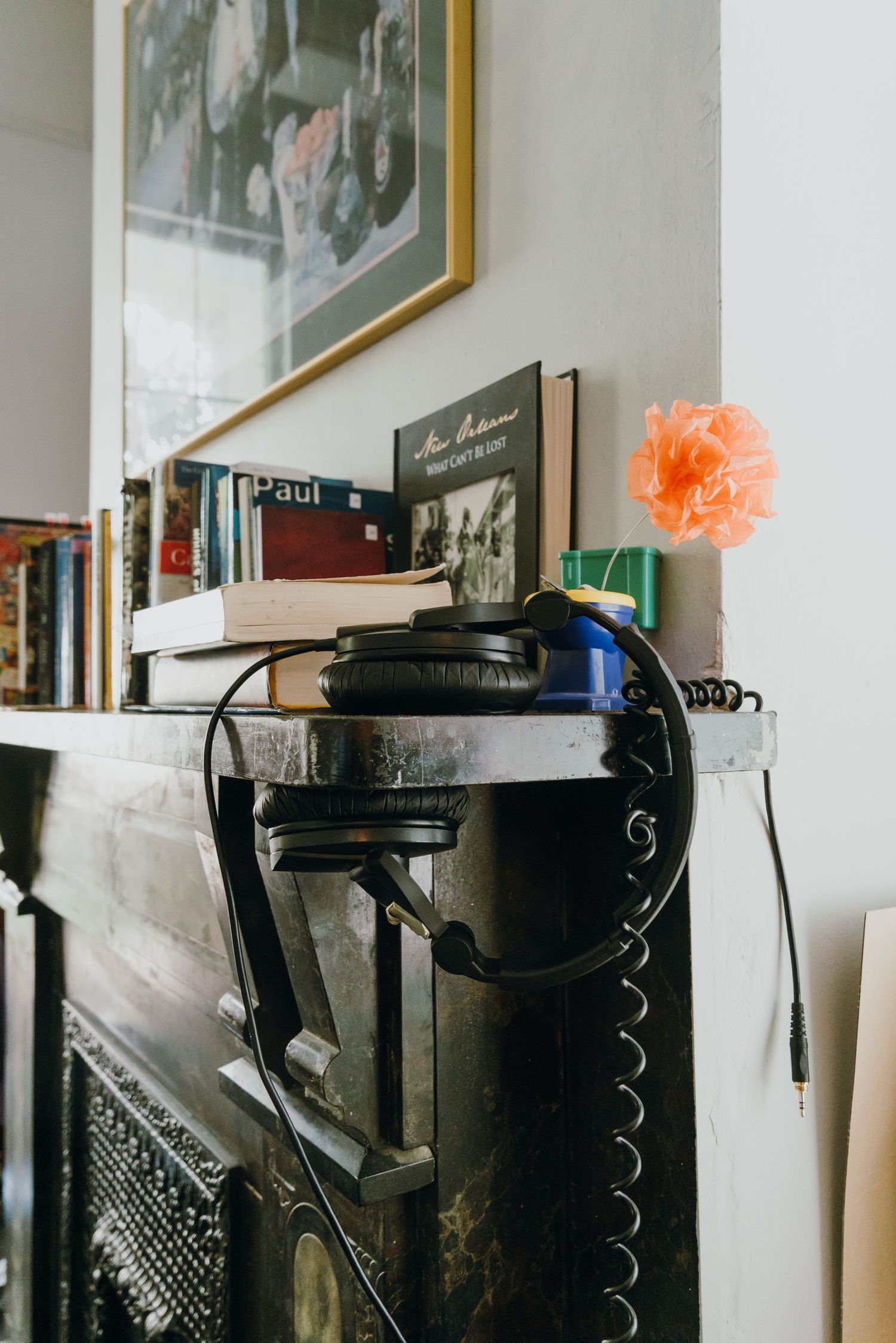 Vintage piano topped with headphones, stacked books, and an orange flower in a cozy home setting.