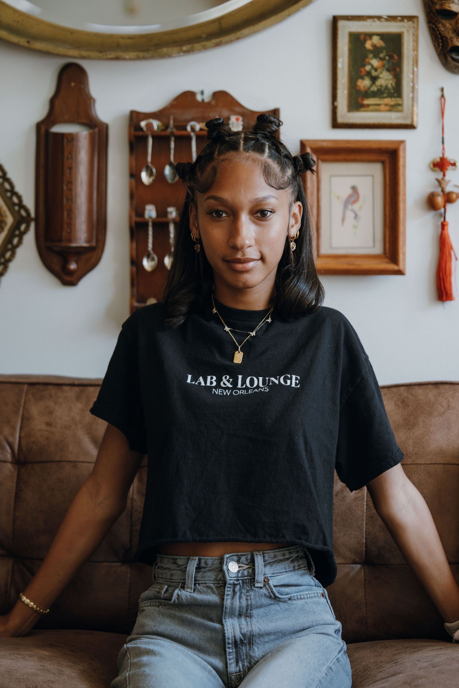 Young woman wearing Lab & Lounge New Orleans black crop tee seated on vintage sofa.