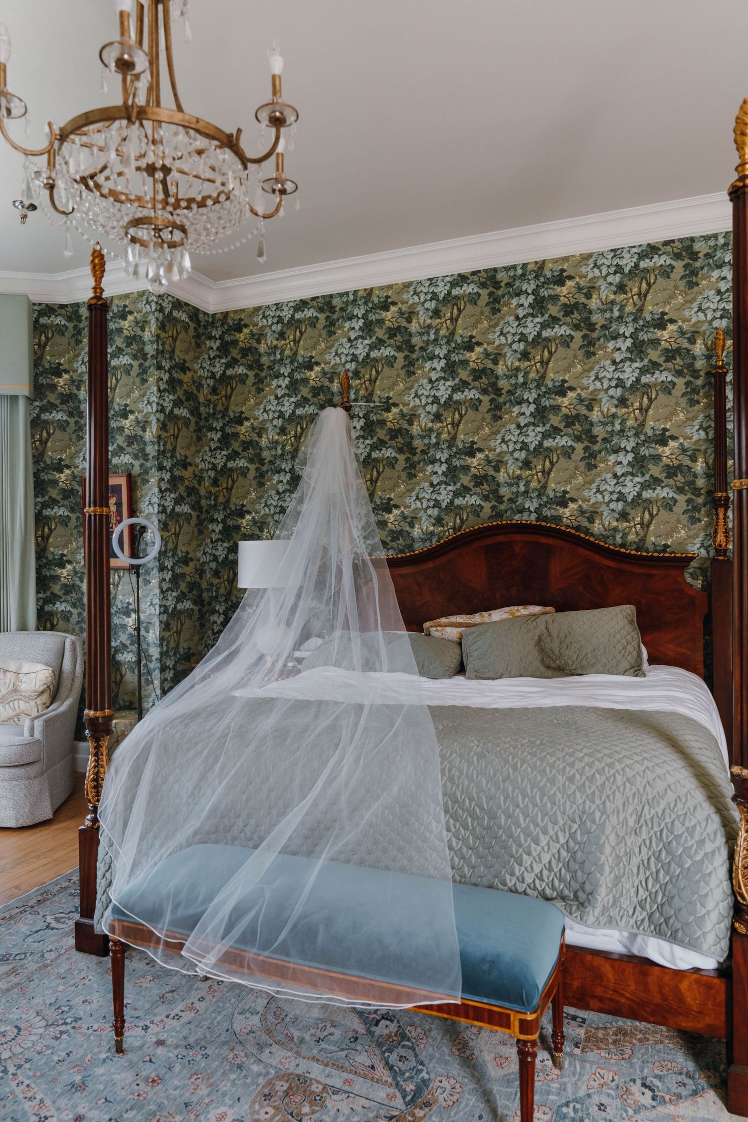 Elegant four-poster bed with bridal veil draped over it in room with green floral wallpaper.
