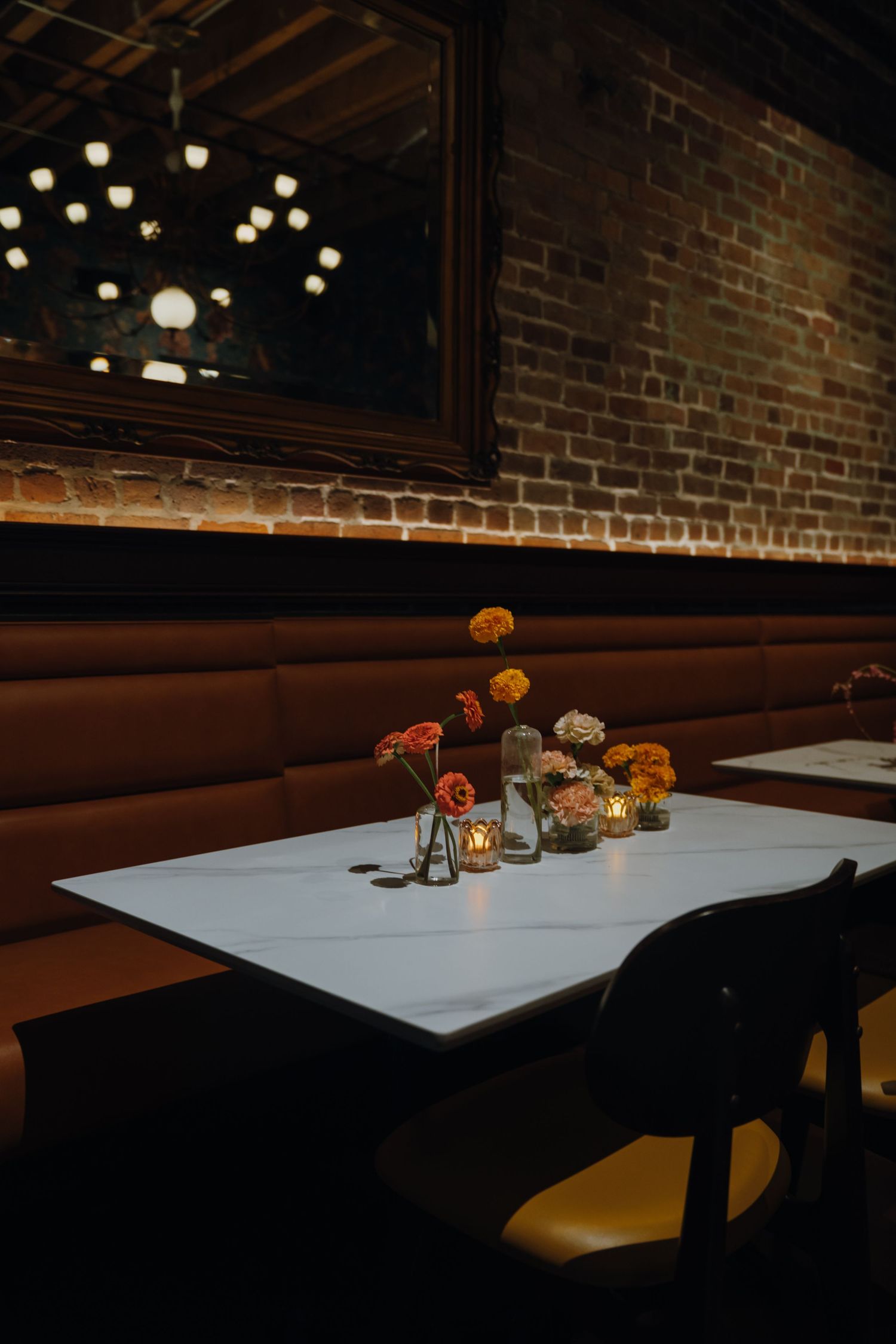 Cozy restaurant booth with brick walls, floral centerpieces, candles, and vintage mirror decor.