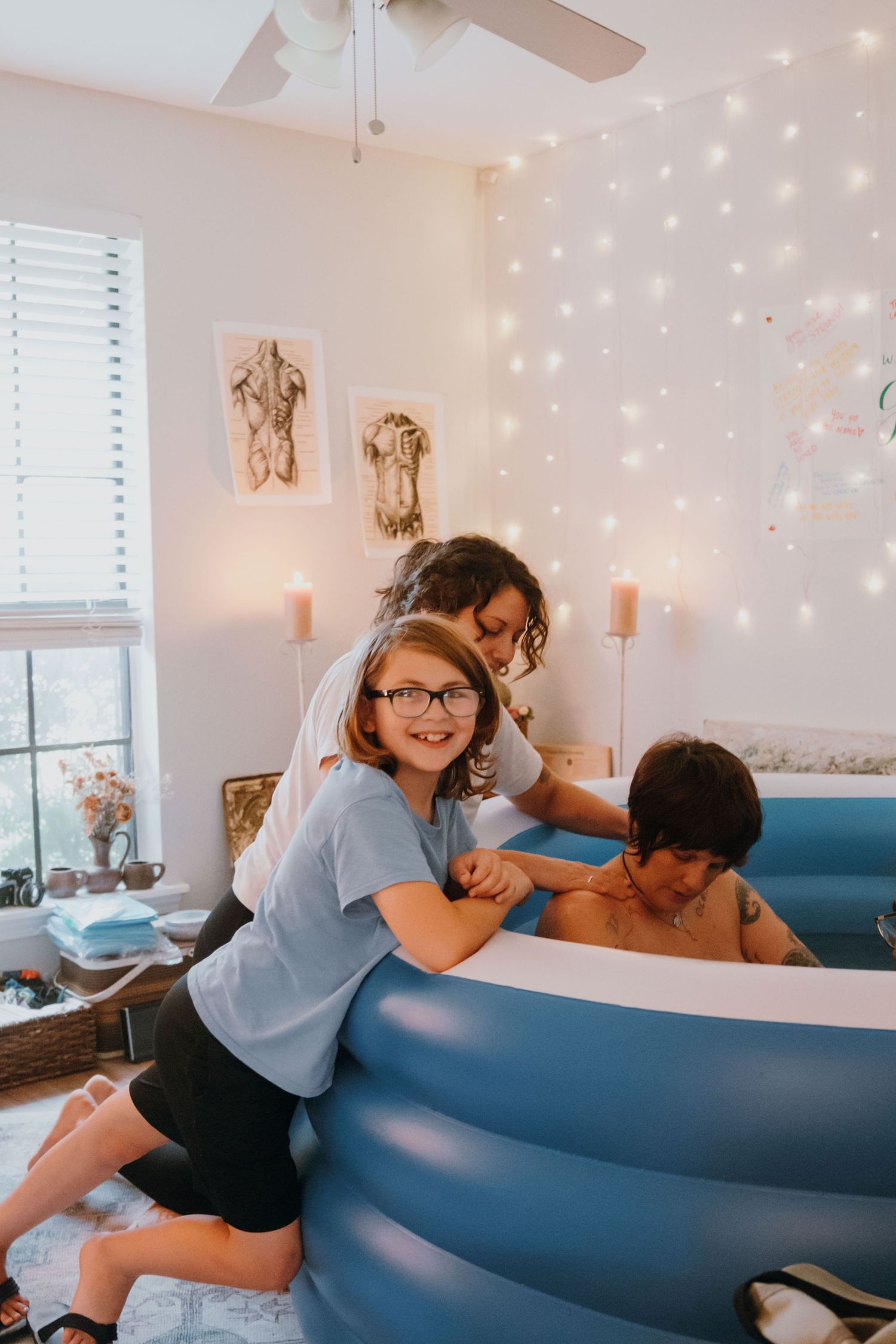 Young girl and woman assist during a home water birth in a blue inflatable birthing pool.