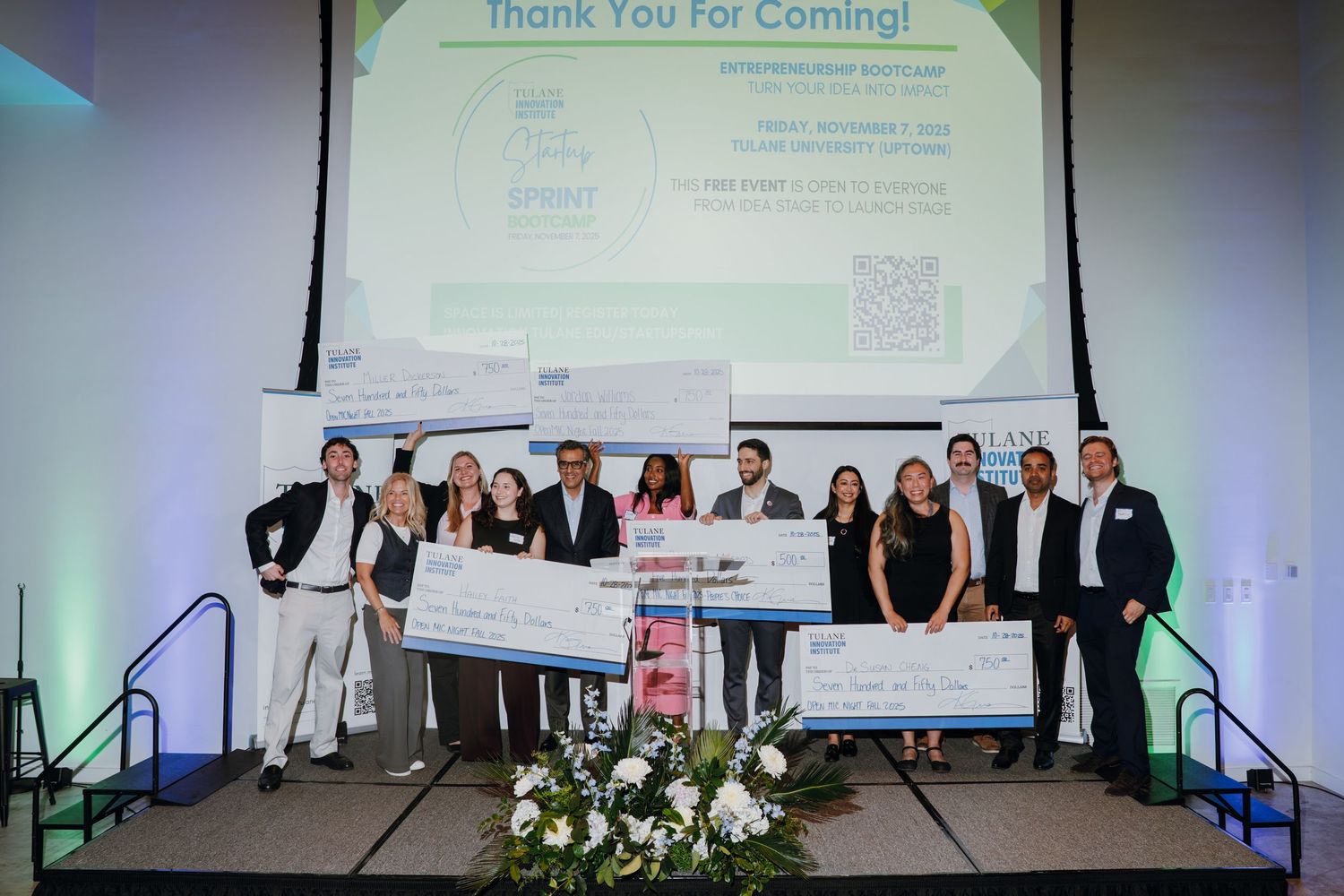 Group of entrepreneurs celebrating on stage holding large prize checks at a business pitch competition event.
