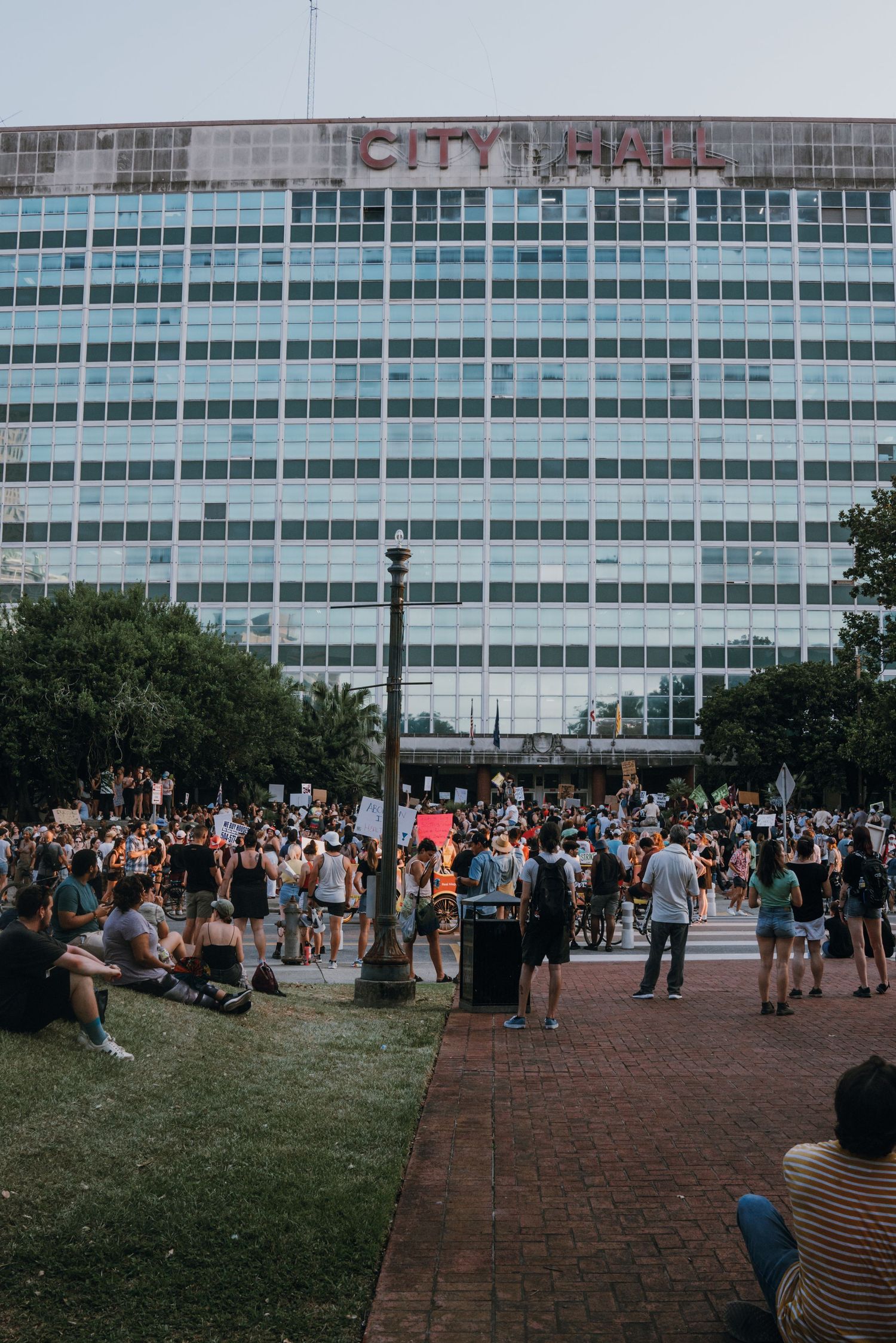 A large crowd gathered in front of City Hall building during an outdoor protest.