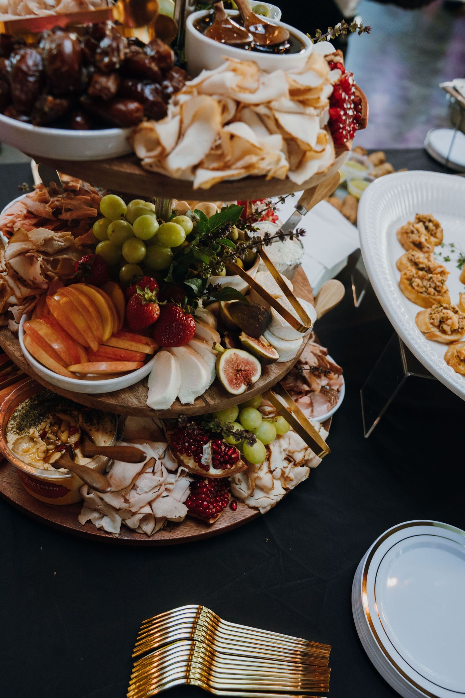 Luxurious three-tier charcuterie board with grapes, figs, cheese, fruits, and assorted crackers.