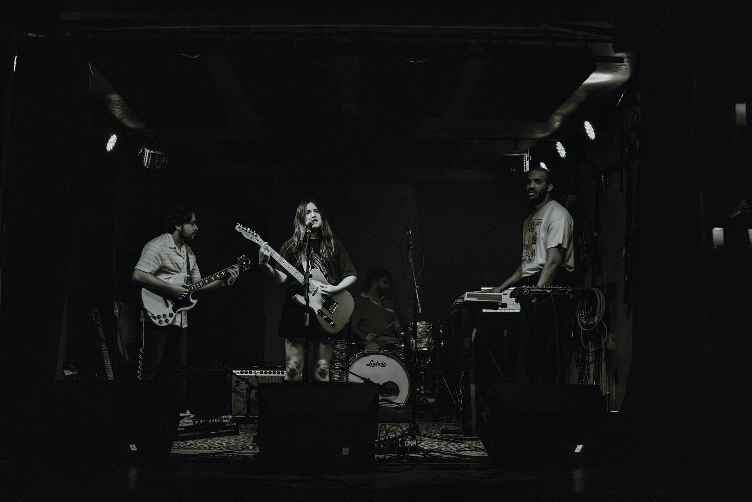Black and white wide shot of a three-piece band performing on a dark indoor stage.