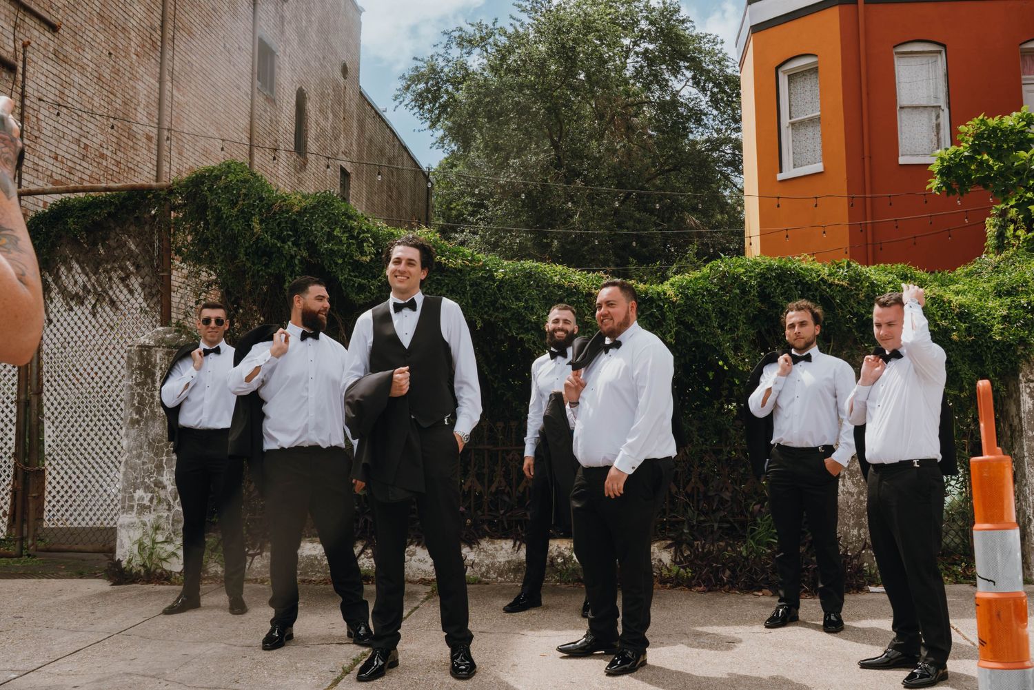 Groomsmen in black and white tuxedos posing casually outdoors before the wedding ceremony.