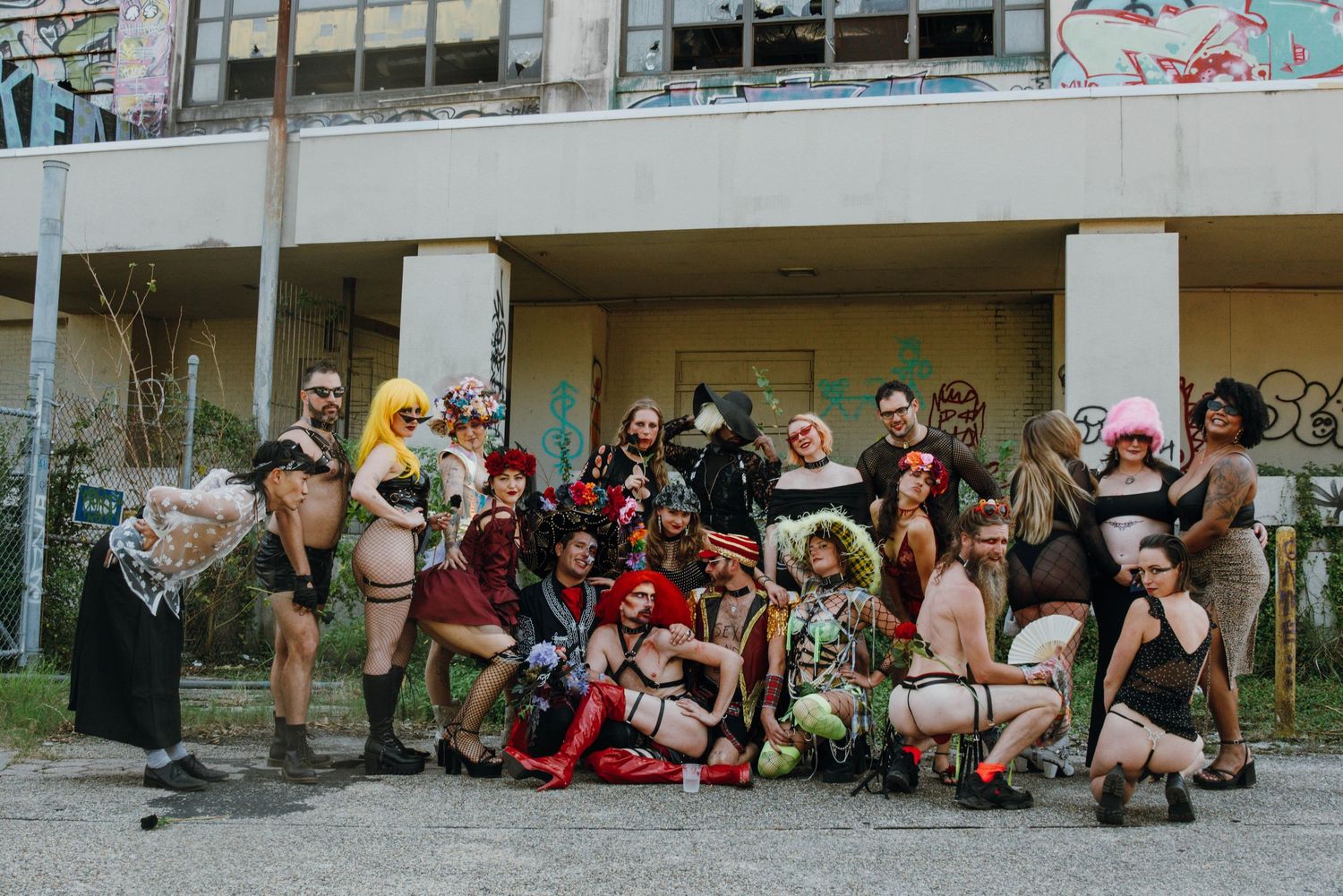 Group of performers in colorful costumes posing in front of a graffiti-covered building.