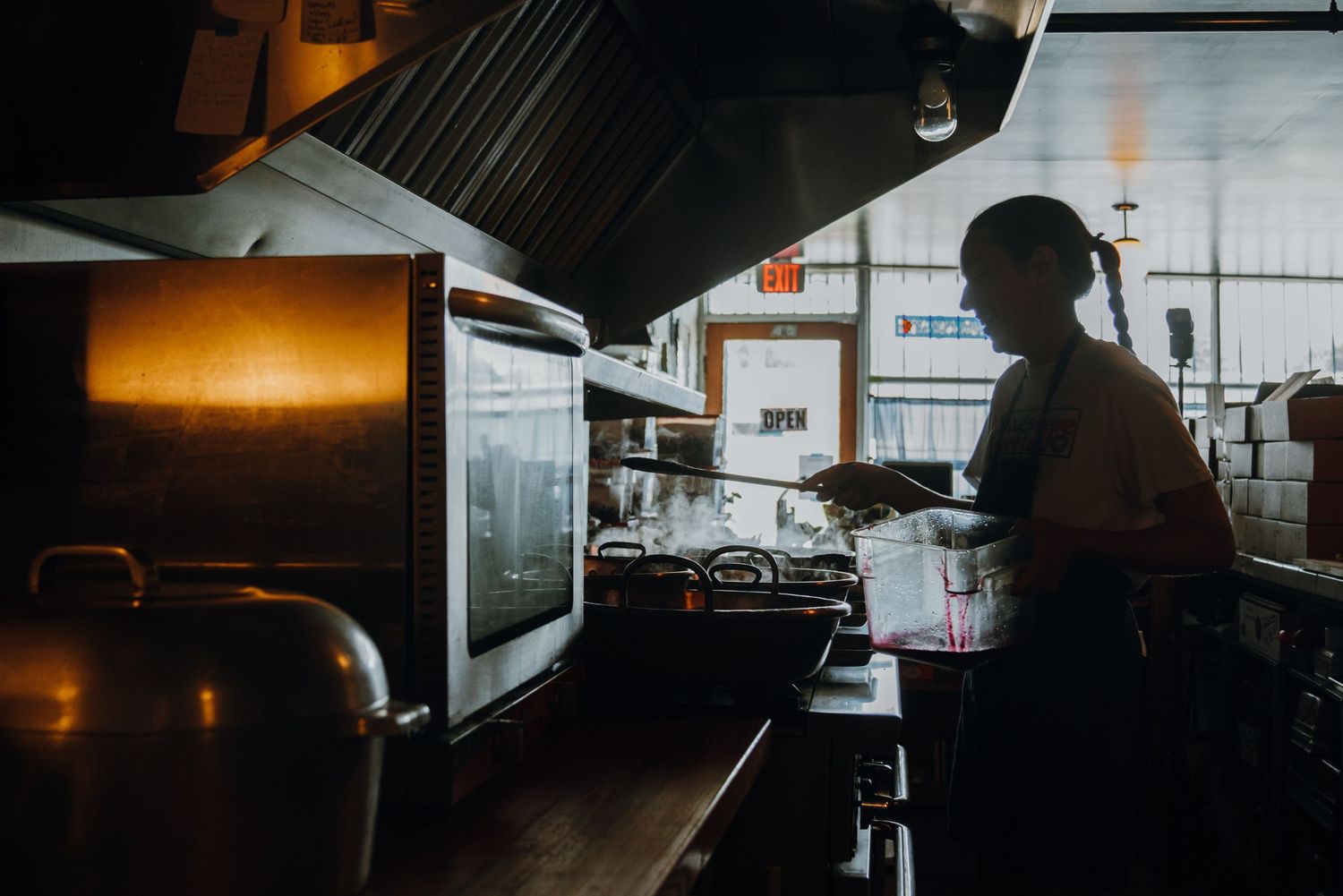 Silhouette of a chef working at a commercial kitchen station under industrial ventilation hood.