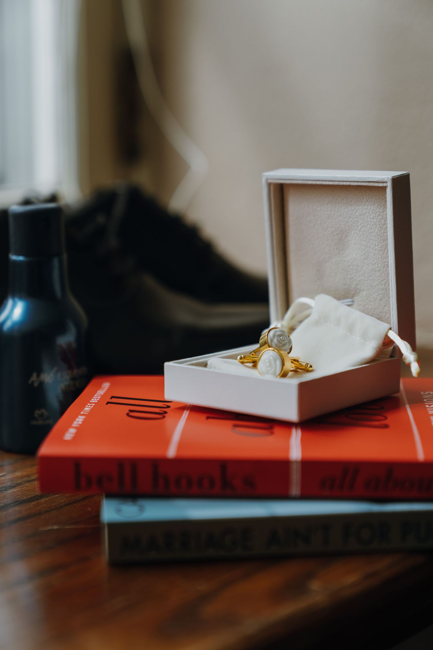 Gold cufflinks in white gift box displayed on stack of red bell hooks books on wooden table. New Orleans, Louisiana, Mississippi