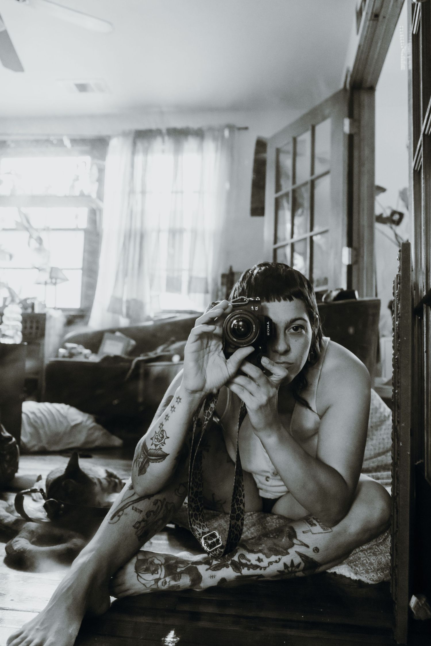 Tattooed photographer taking self-portrait with DSLR camera sitting on floor in black and white. New Orleans, Louisiana, Mississippi