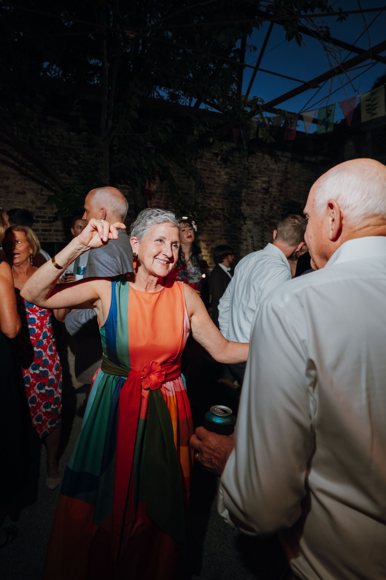 Joyful woman in colorful rainbow dress dancing with partner at lively outdoor evening wedding reception.