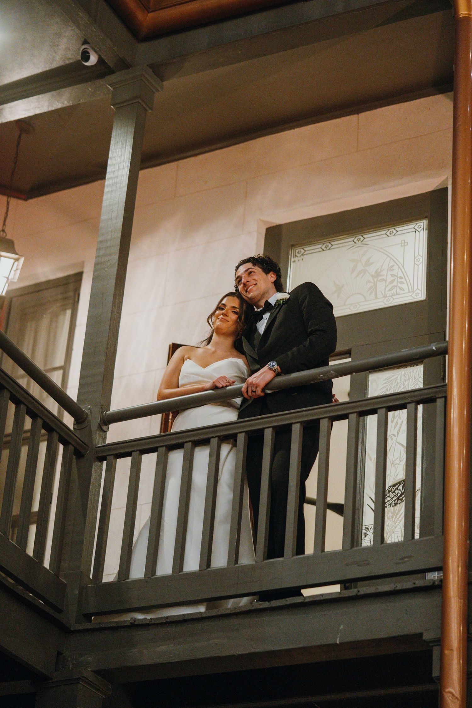 Bride and groom sharing romantic moment on balcony of historic venue after wedding ceremony.