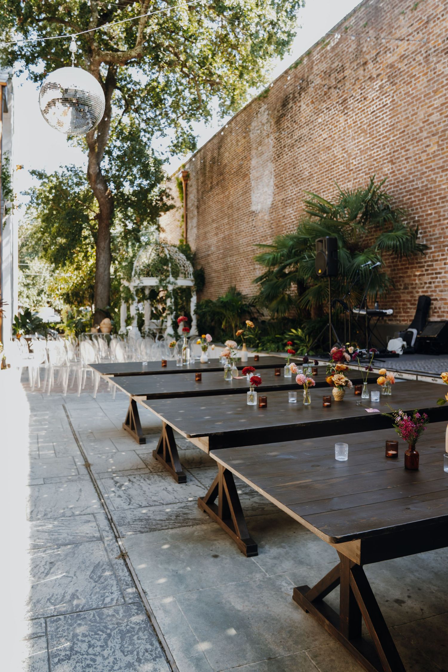 Outdoor wedding reception with long dark wood farm tables decorated with colorful floral centerpieces.