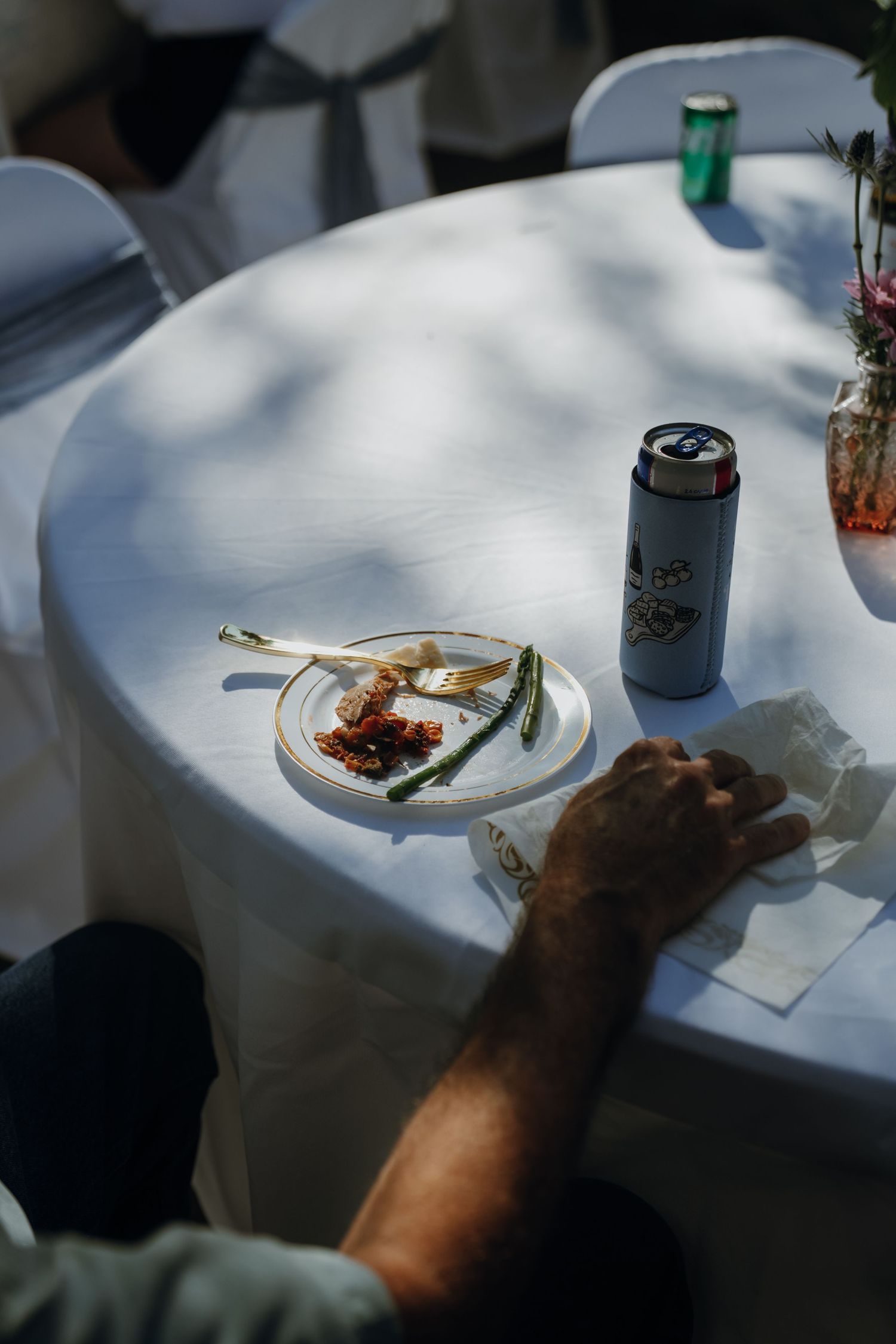 Close-up of a plate with asparagus and food remnants beside a slim can on a white tablecloth.