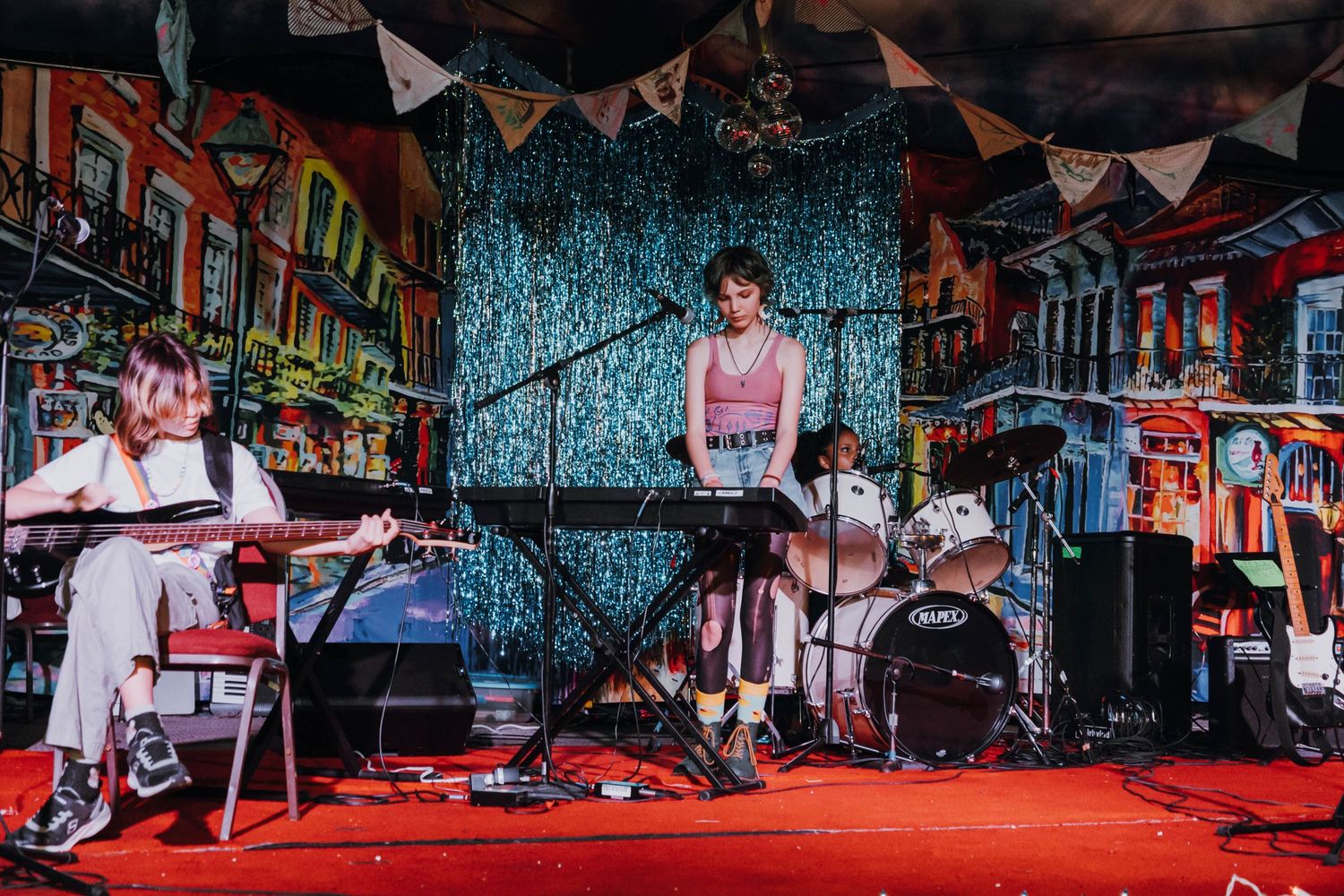 Two young musicians performing on stage with guitar and keyboard at a colorful venue.