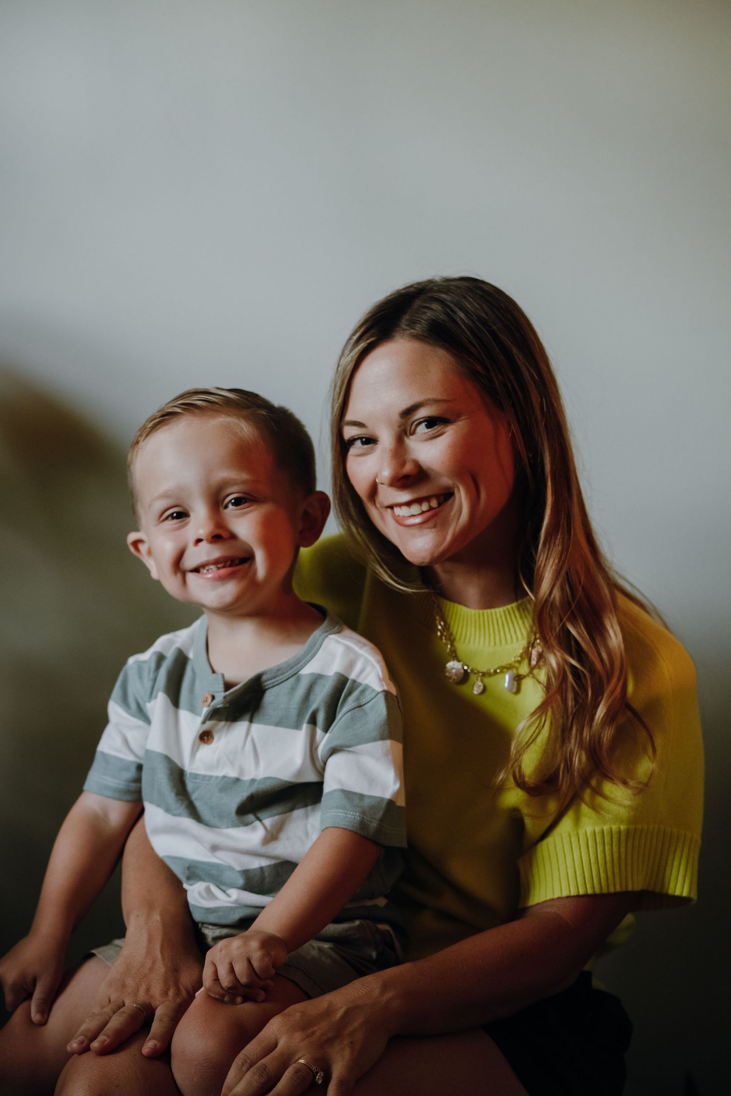 Happy mother and young son smiling together in a bright indoor portrait photograph.