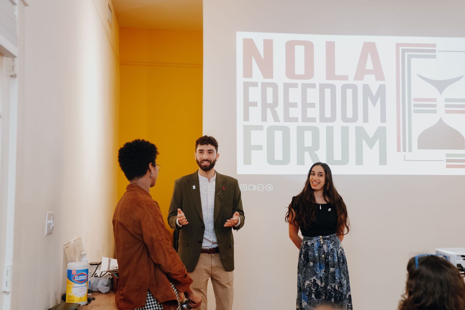 Three speakers present at the NOLA Freedom Forum event in front of a projected logo.
