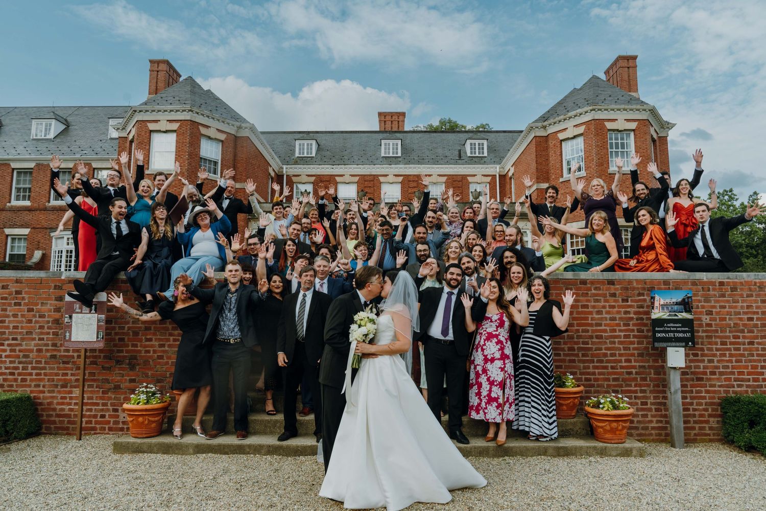 Wedding couple kissing before cheering guests outside elegant red brick estate venue.