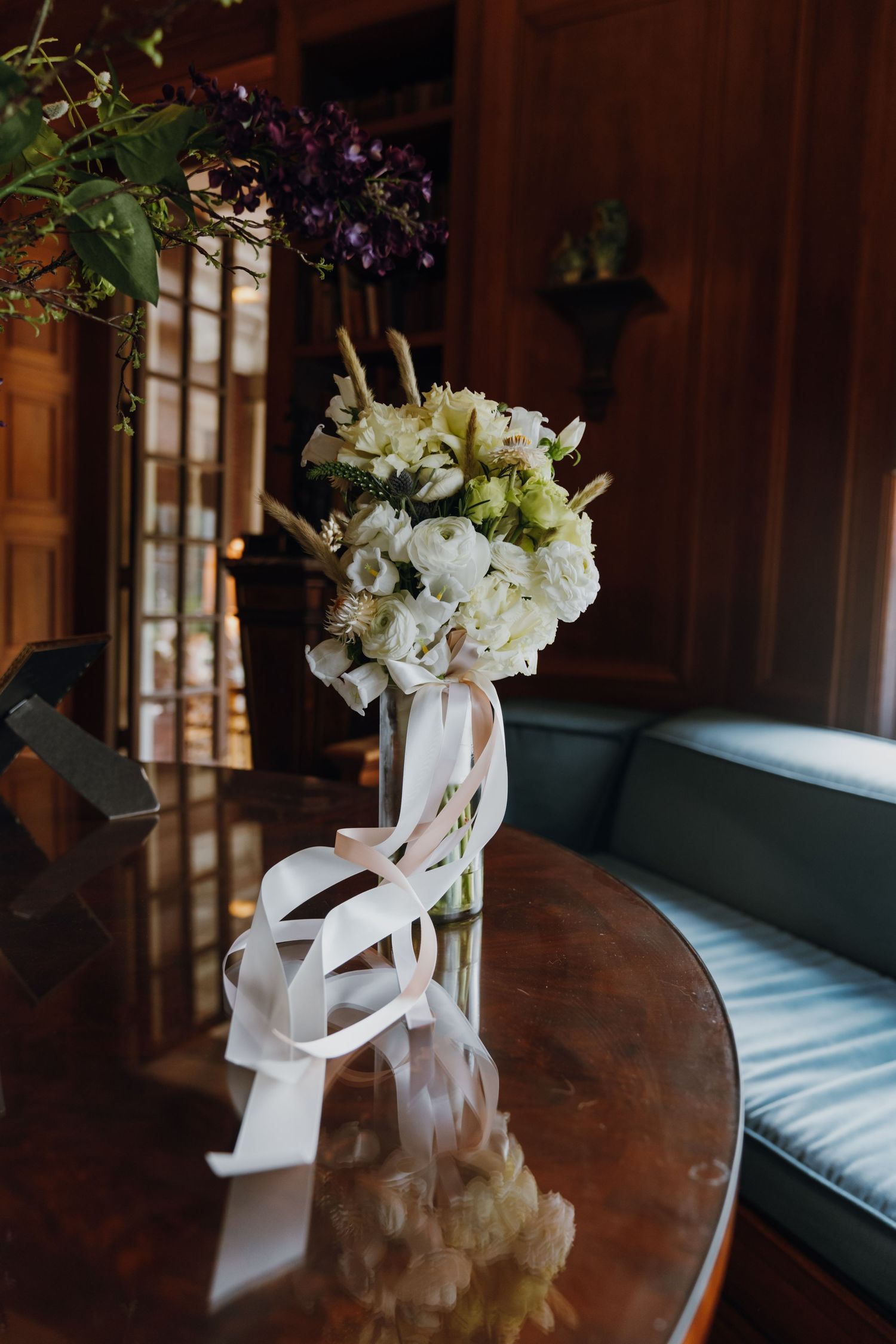Elegant white bridal bouquet with ribbon streamers displayed in vase on wooden table in dark room. New Orleans, Louisiana, Mississippi