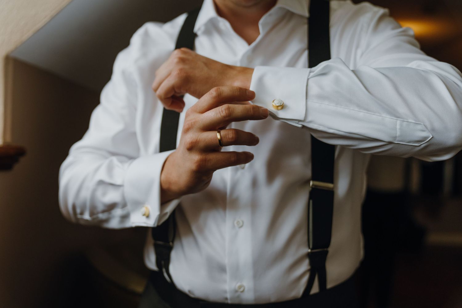 Groom in white dress shirt and suspenders fastening gold cufflinks on his wedding day. New Orleans, Louisiana, Mississippi