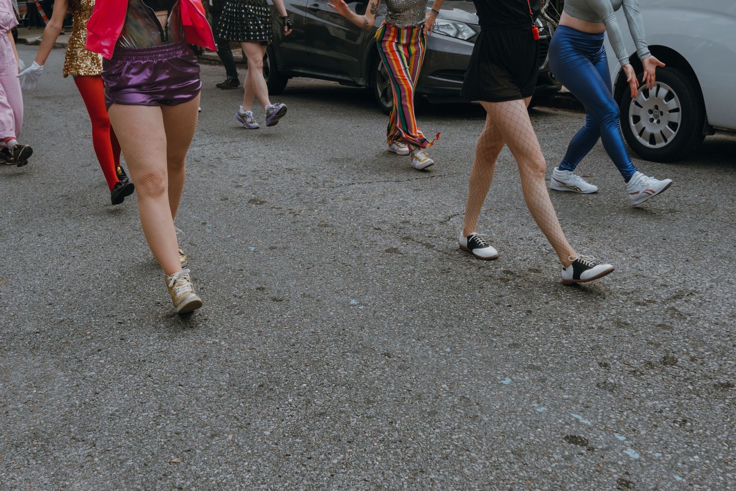 Close-up of dancers legs in colorful outfits stepping in unison on an urban street.