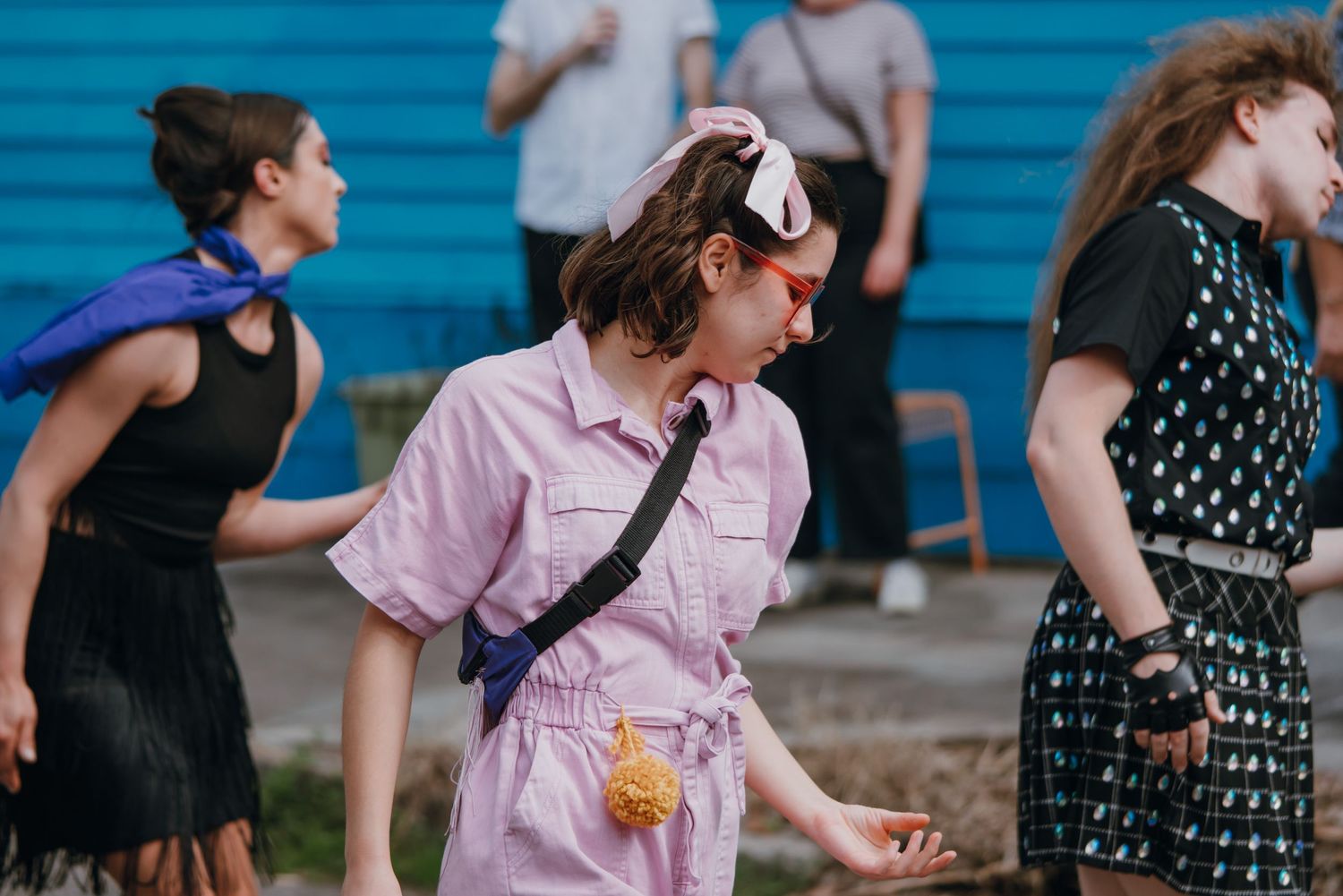 Person in pink jumpsuit dancing outdoors near a blue wall at a street event.