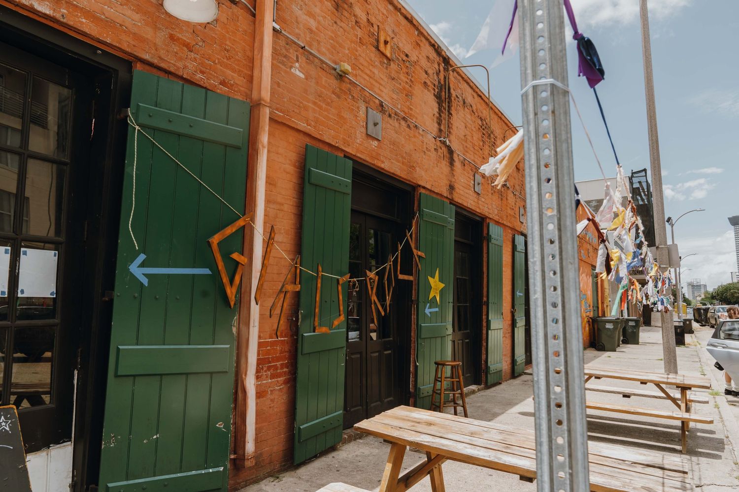 Rustic brick building exterior with green doors, wooden benches, and colorful hanging banner decorations.