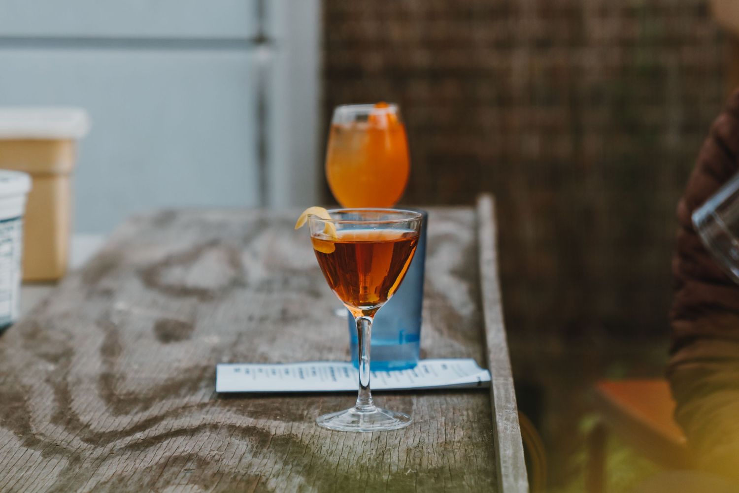Two elegant cocktails on a rustic table, one in a coupe glass with citrus garnish and another with an orange slice.