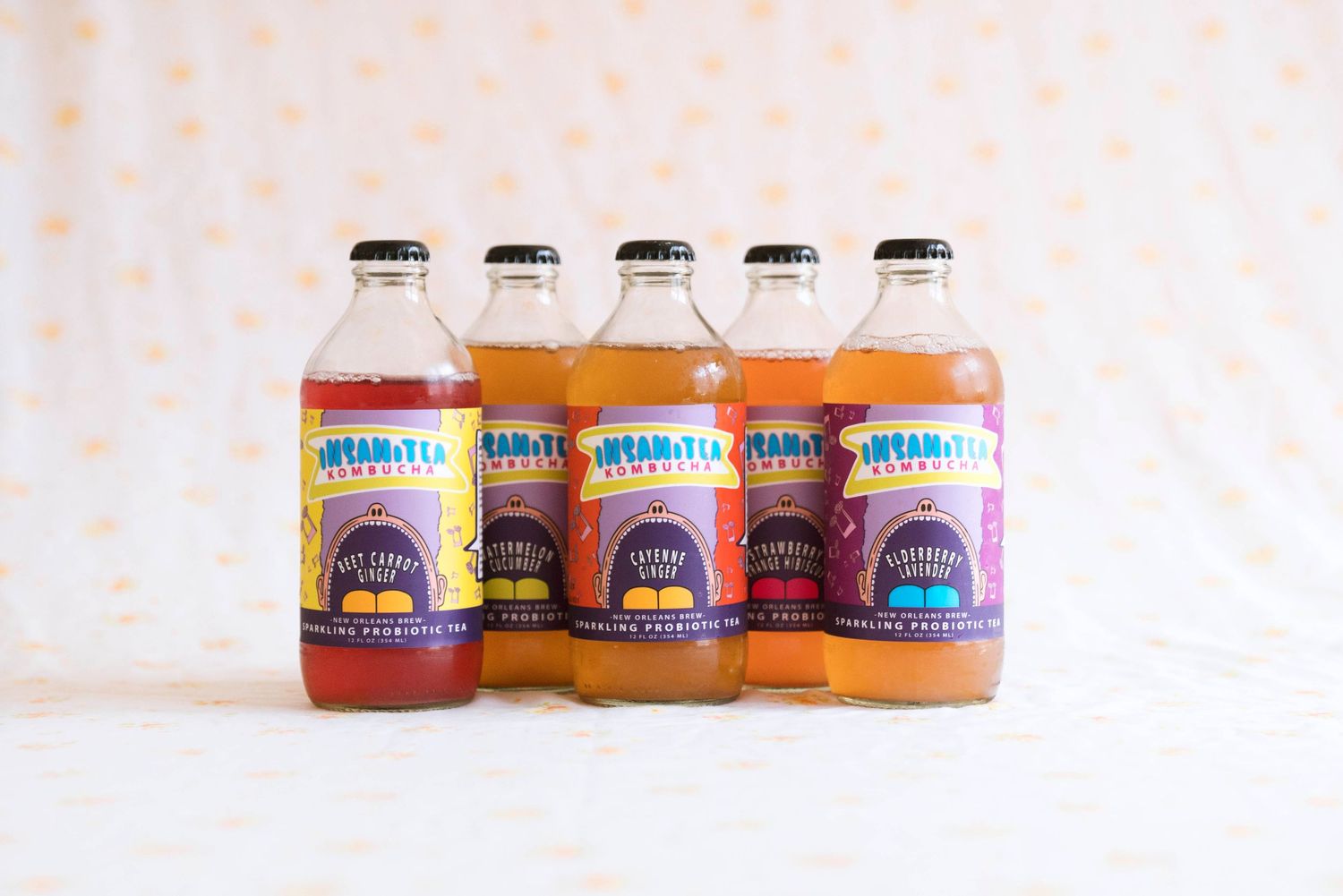Five bottles of Insani-Tea Kombucha sparkling probiotic tea lined up against a polka dot background.